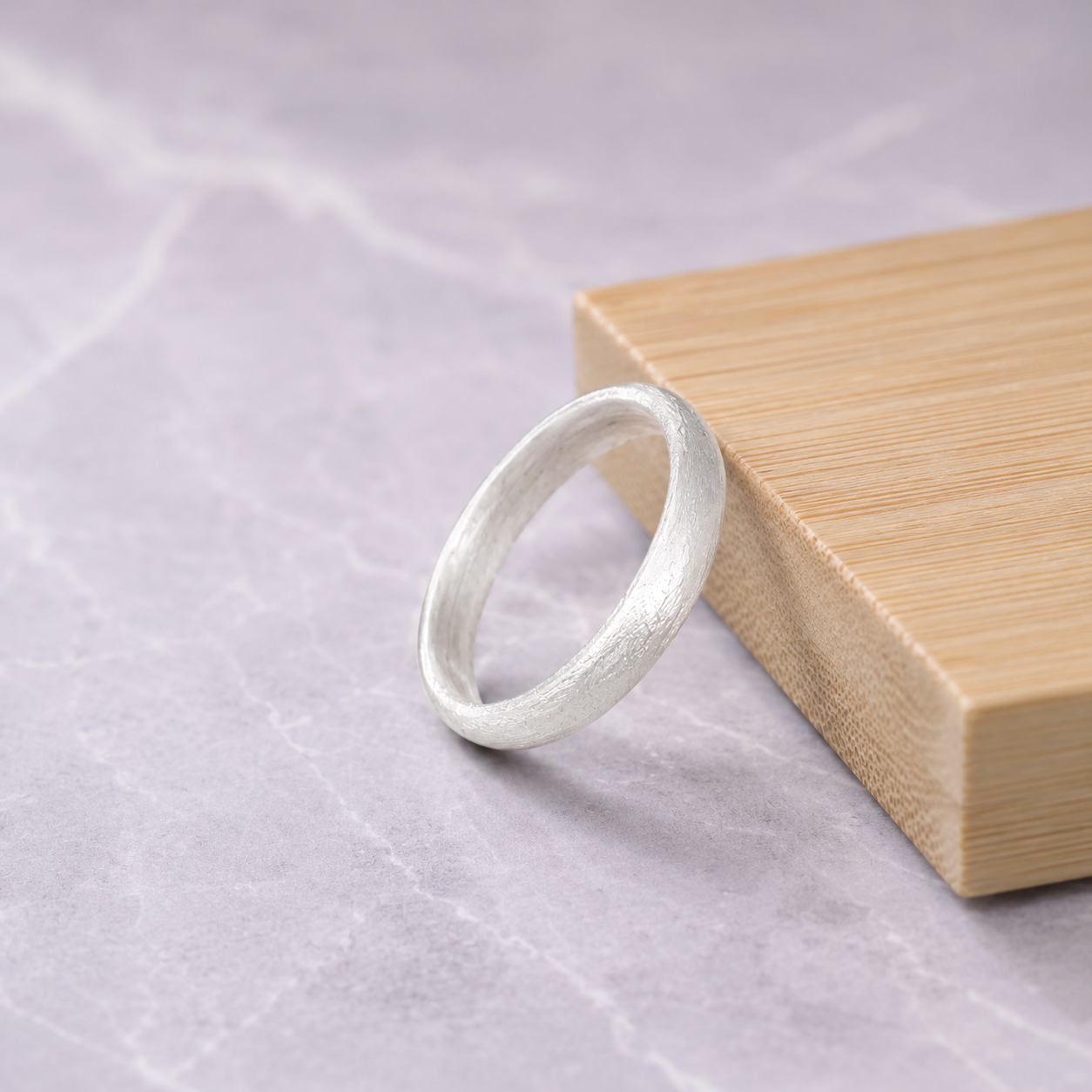 Handmade brushed 999silver wedding band resting against a wooden block on a marble surface.