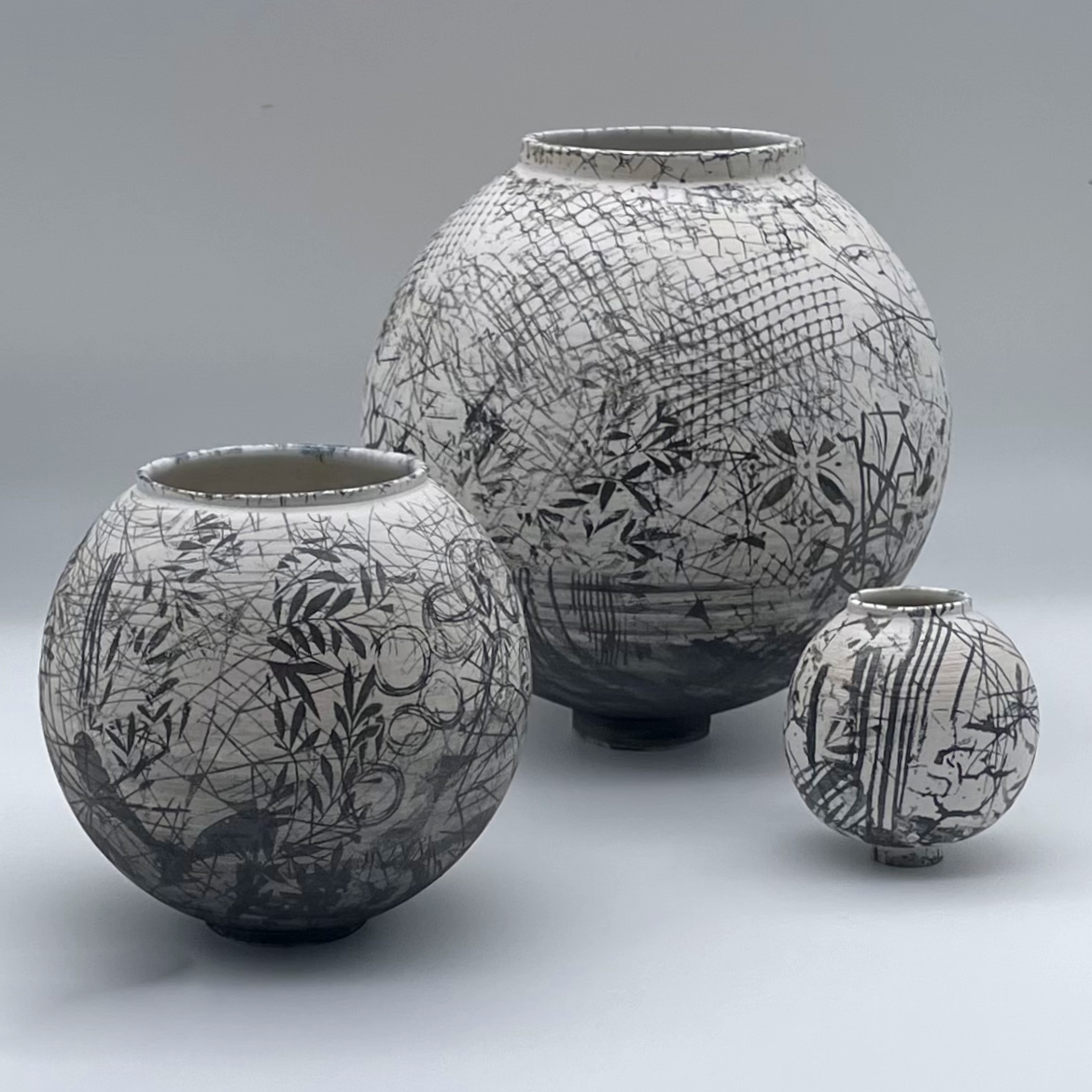 3 ceramic moon jars which are different sizes with abstract black and white pattern on the surface