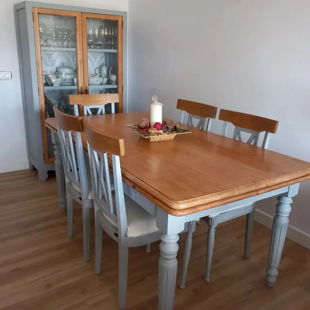 una mesa color madera y cinco sillas color gris con una vitrina de fondo del mismo color