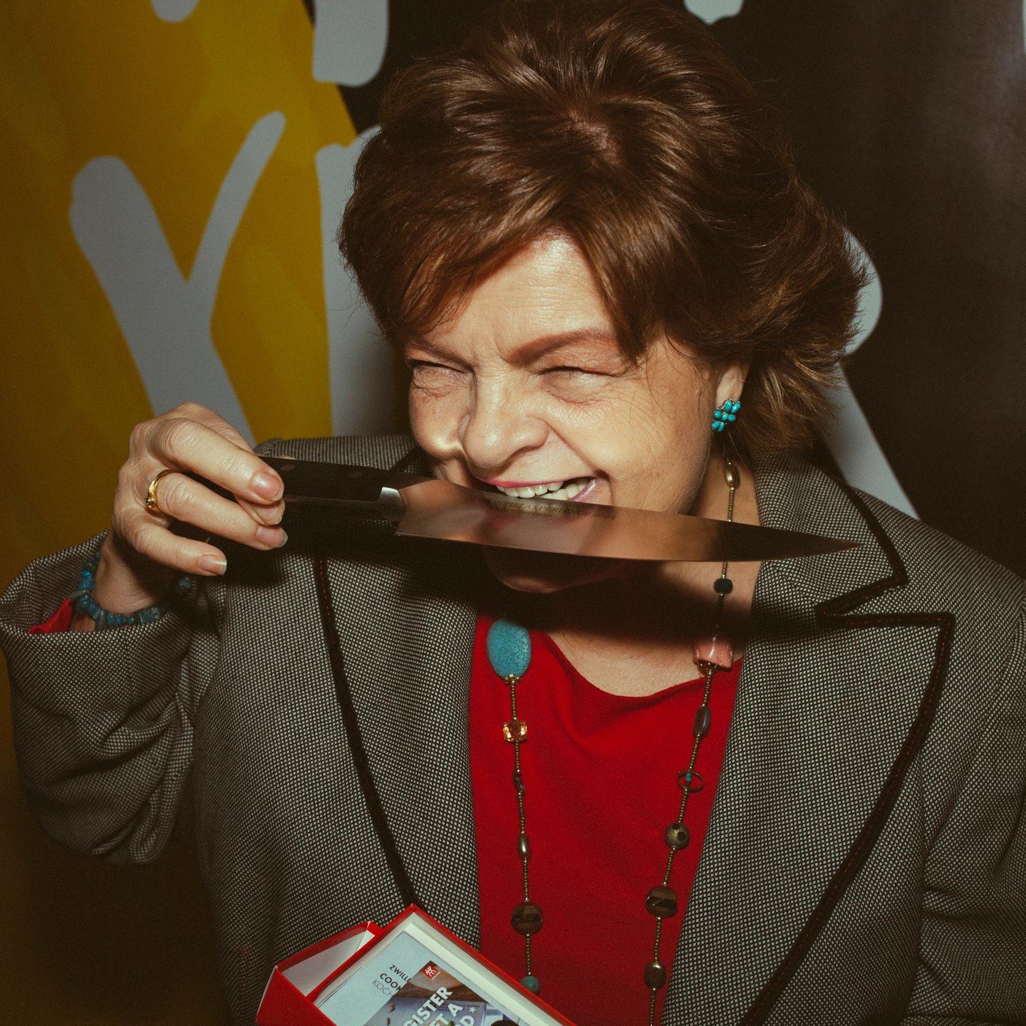 Mujer mayor divertida mordiendo un cuchillo y riendo para la marca de cuchillos Zwilling