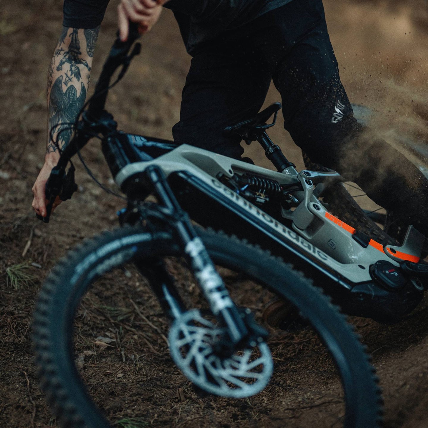 Tattooed rider cornering a Cannondale electric mountain bike on a dirt trail.