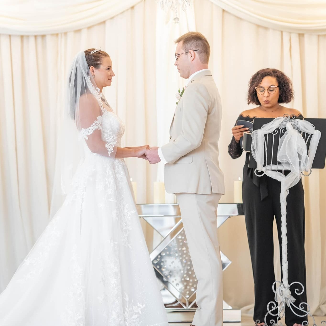 Bride and groom exchange wedding vows during an elegant indoor ceremony with a female officiant.