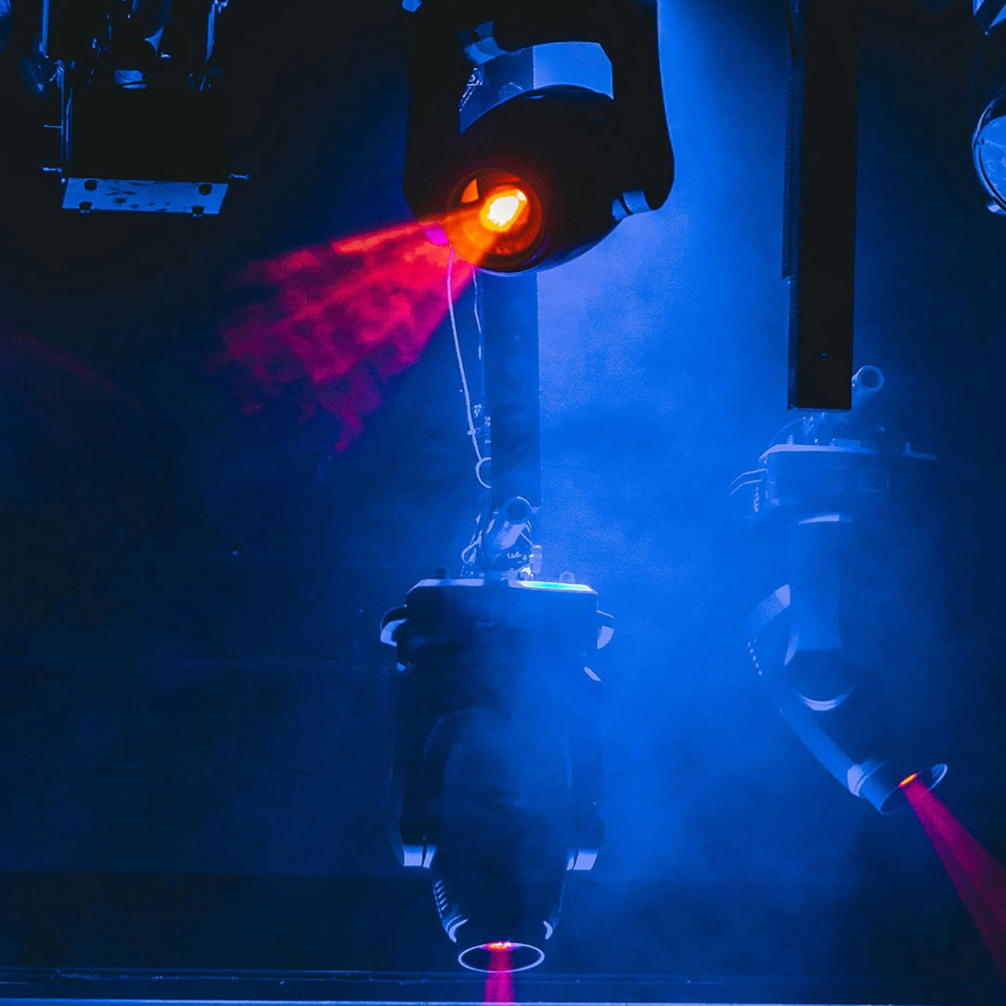 Professional stage lighting equipment casting red laser beams through blue concert fog.