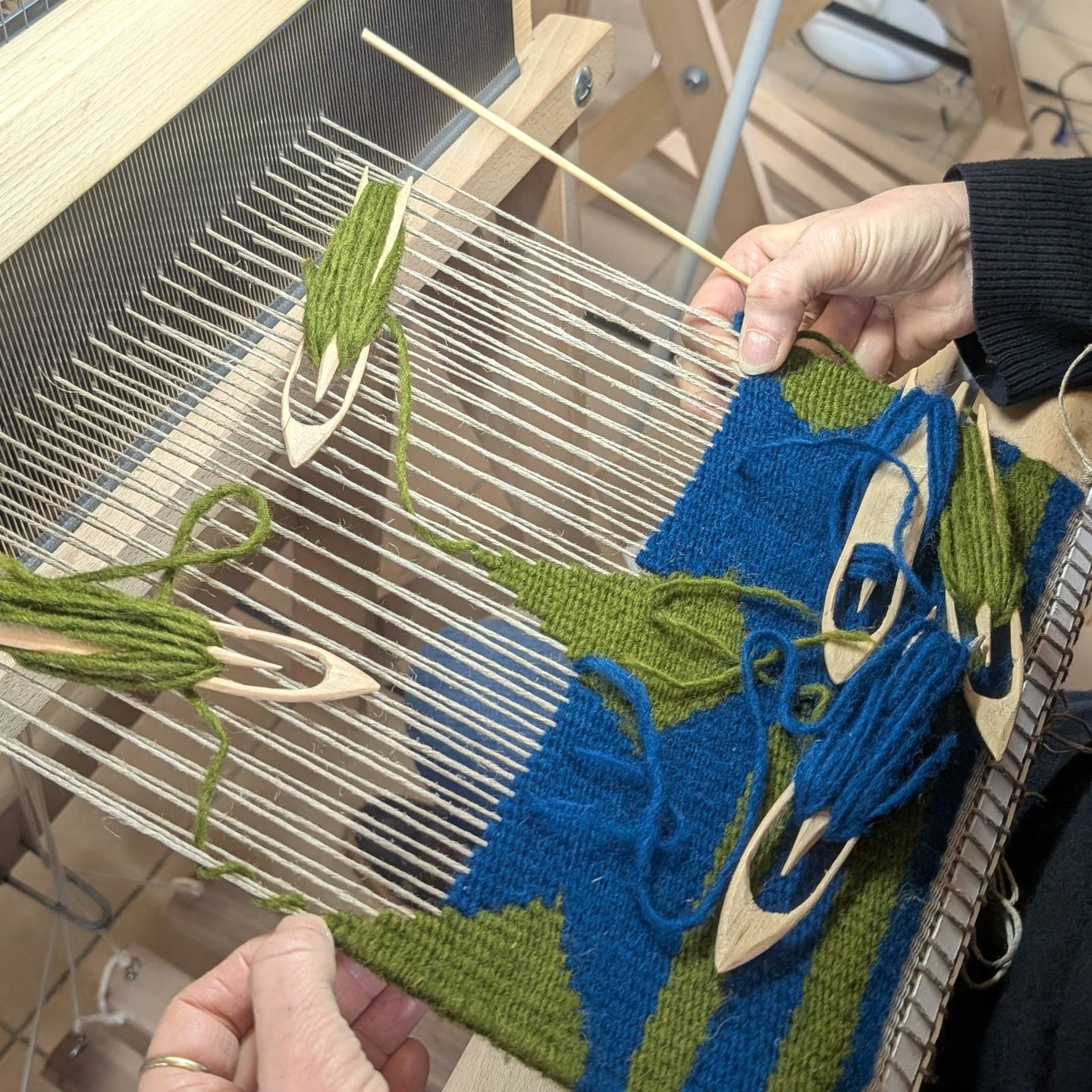 Stagiaire tissant un kilim géométrique en bleu et vert sur un métier à tisser avec navettes