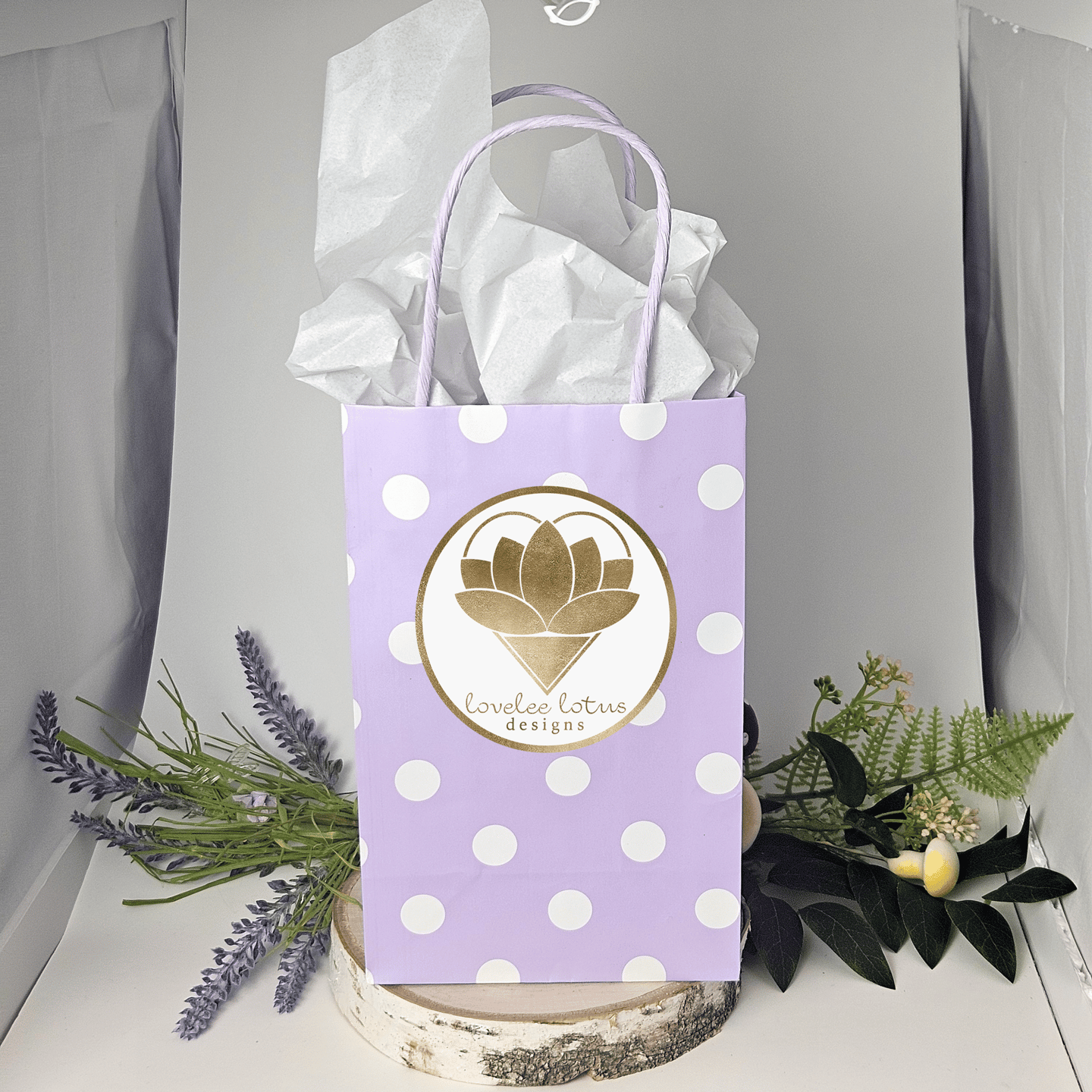 A purple gift bag with white dots and the Lovelee Lotus Designs logo