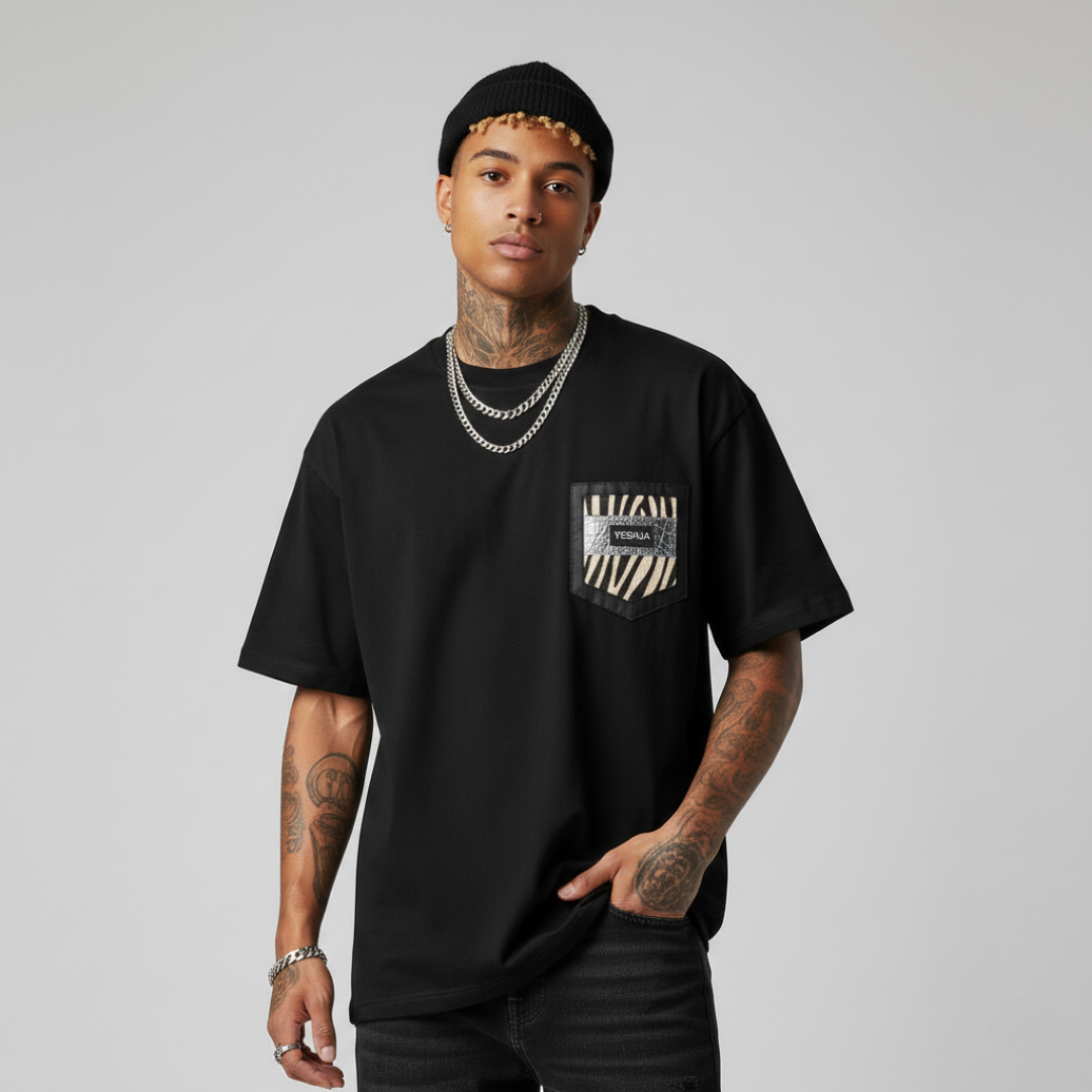 A man wearing a black streetwear t-shirt with a zebra print pocket and silver chain necklaces.