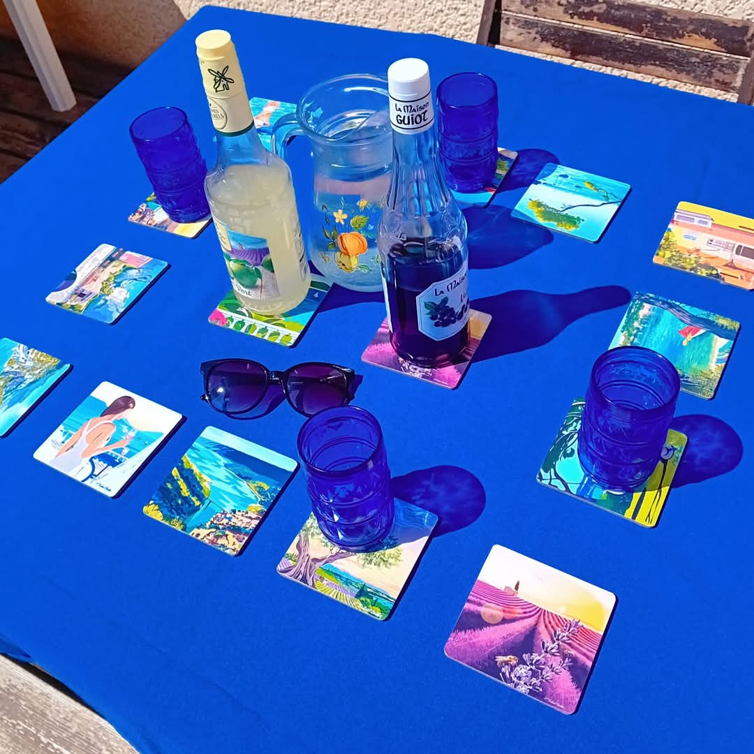 Dessous de verres paysages de Provence Realisart sur une nappe bleue.