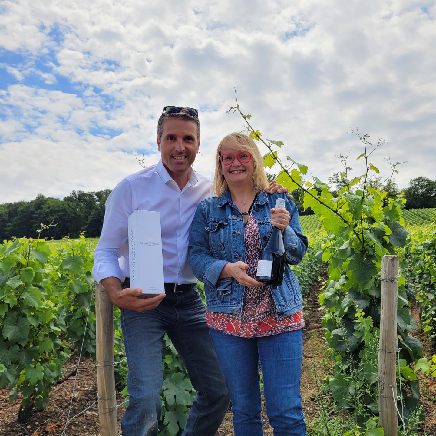 Patrice et Nathalie dans les vignes présentant la bouteille et l'étui du Champagne La Bulle du Bassi