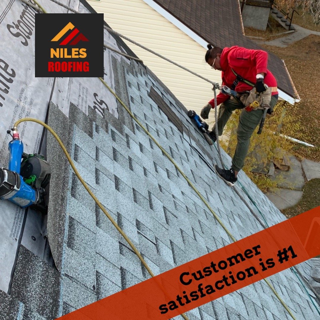 Professional roofing contractor installing new asphalt shingles on a steep residential roof with safety harness.