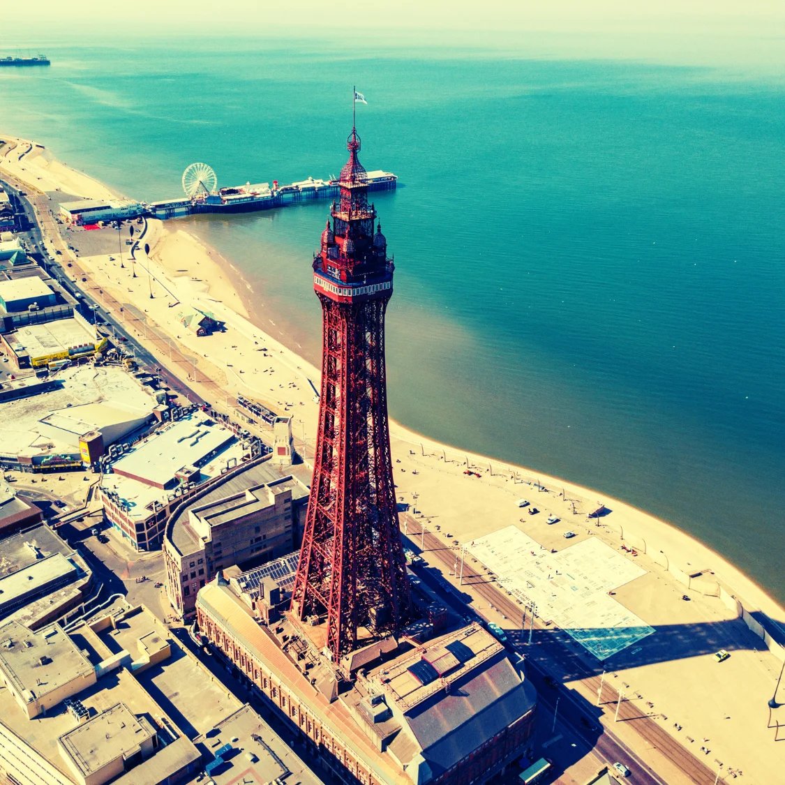 Aerial view of the iconic Blackpool Tower overlooking the sandy golden  beach and the Pier. Sea.