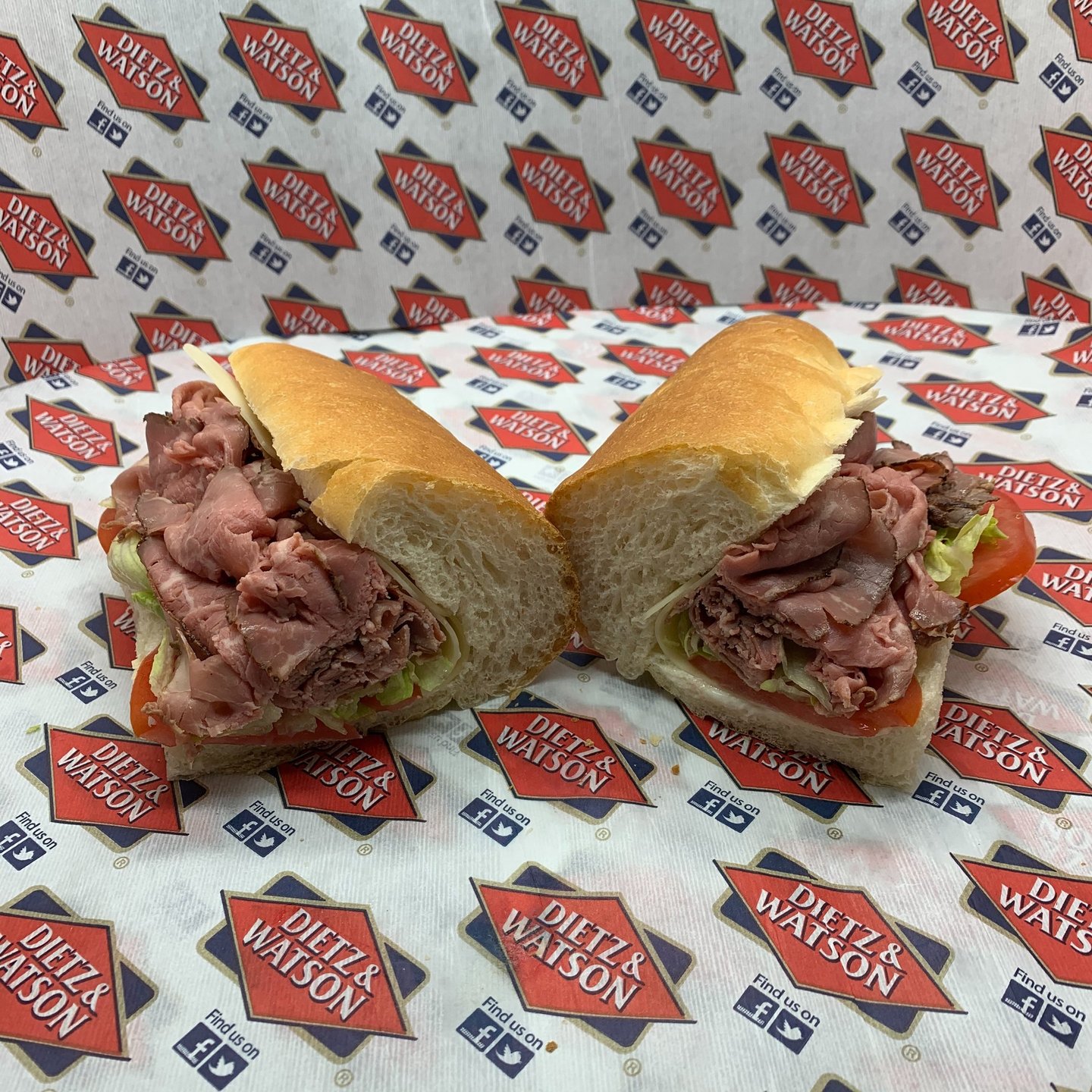 Fresh roast beef deli sub with lettuce and tomato on a long roll atop Dietz and Watson paper.