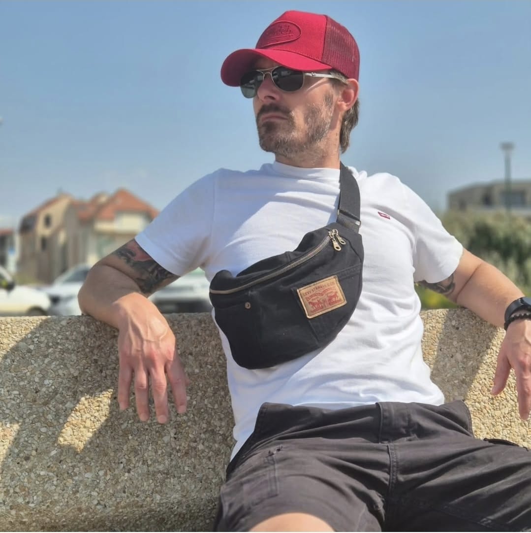 un homme assis portant un sac banane en jean noir recyclé en bandouillère