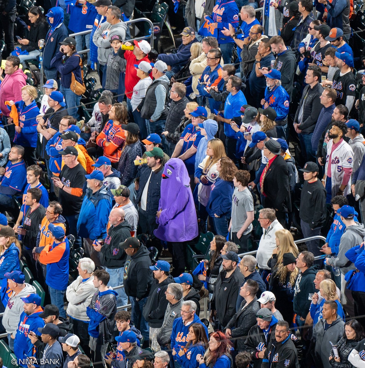 purple grimace standing amongst mets fans in the stands