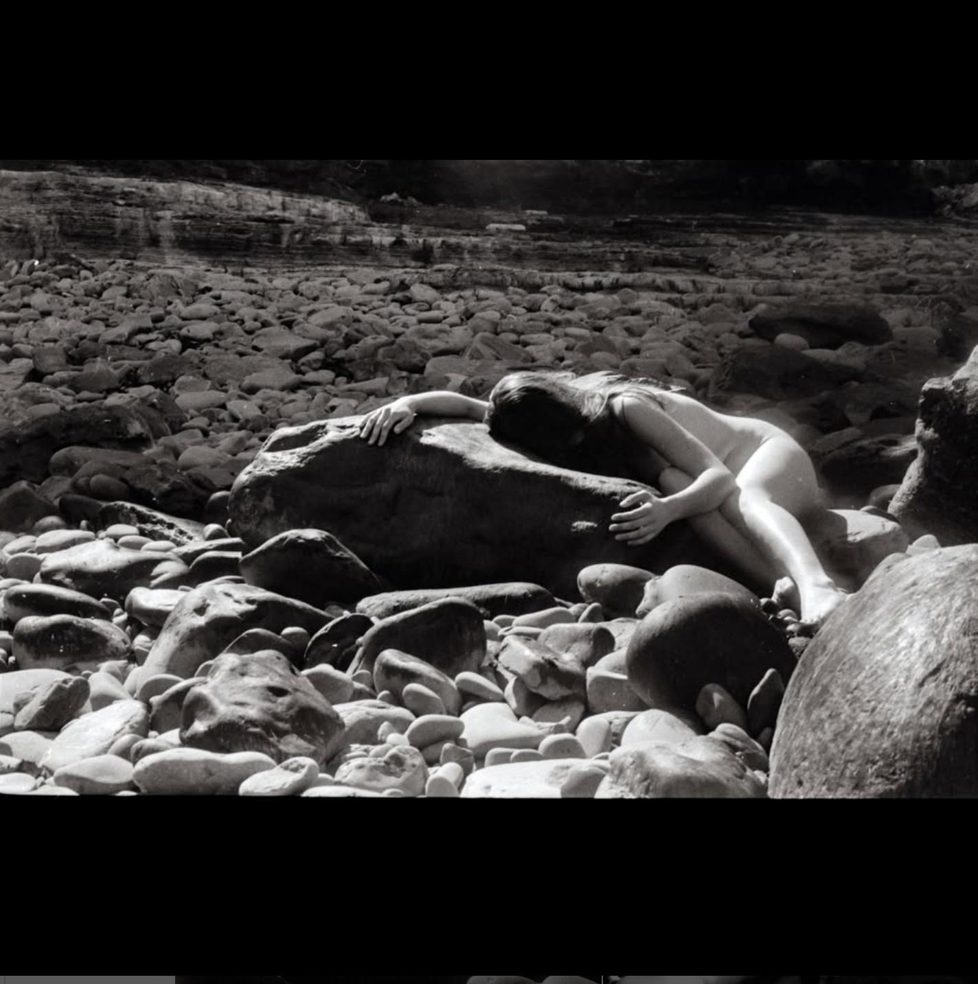 A woman holding and being held by smooth solid rocks surrounded by smaller rock fragments