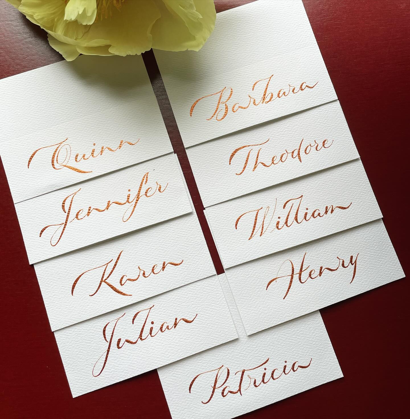 Beautiful calligraphy place cards in metallic bronze ink on white paper showcased on red background 