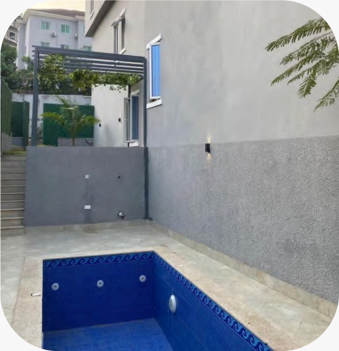 Modern outdoor swimming pool area with blue mosaic tiles and a grey textured wall.
