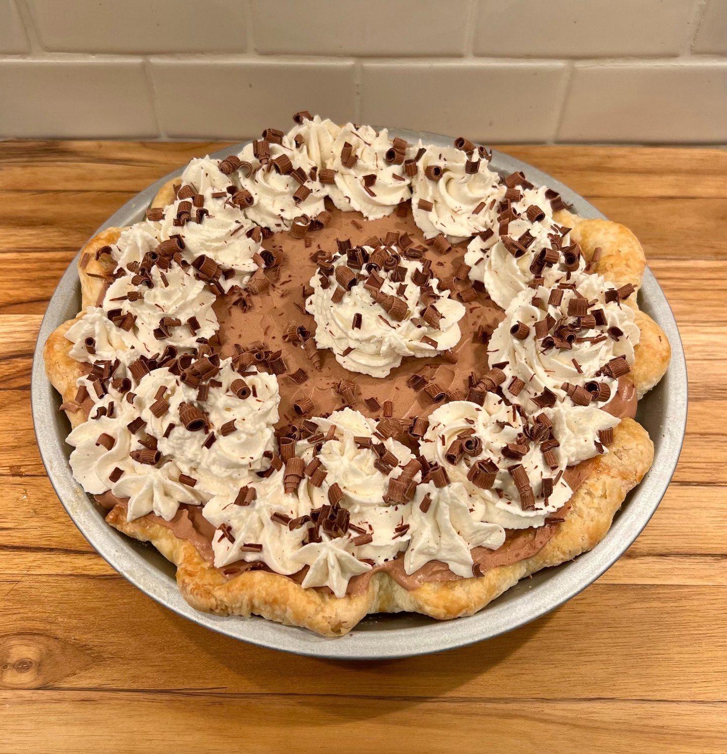 A homemade French silk pie topped with whipped cream swirls and chocolate curls in a flaky crust.