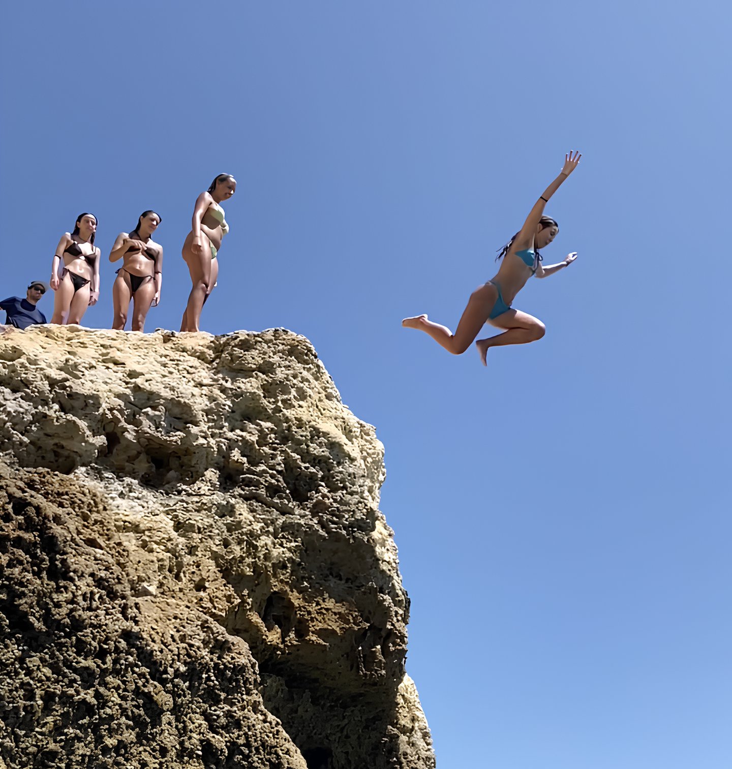 a woman jumping into the water from a cliff