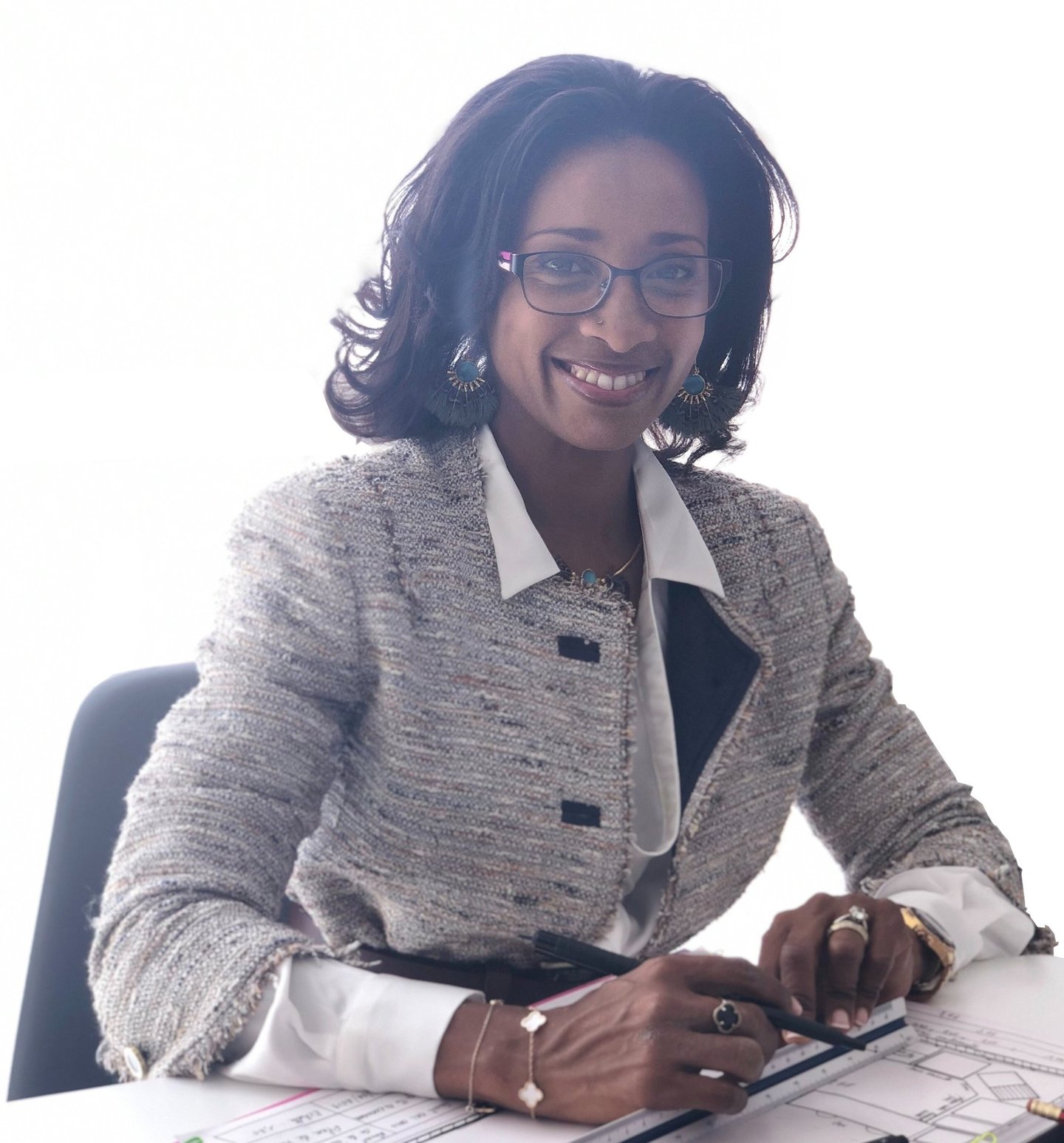 Smiling professional female architect in a blazer working on blueprints at her office desk.