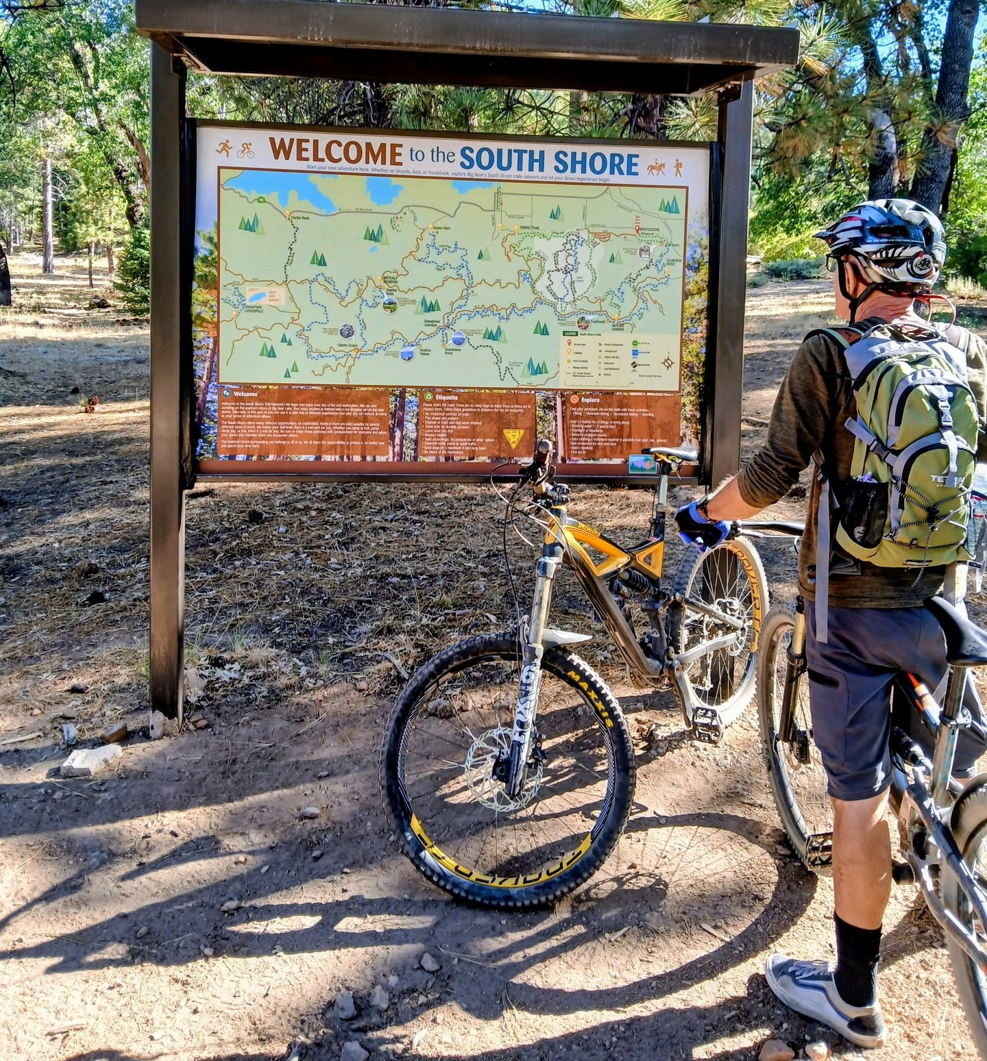 Mountain biker looking at trail map sign while wearing a hydration backpack for a long ride