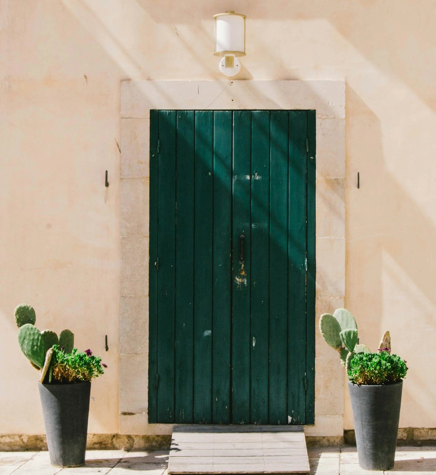 itahome luxury Rustic dark green wooden door on a beige stone wall flanked by potted cactus plants.