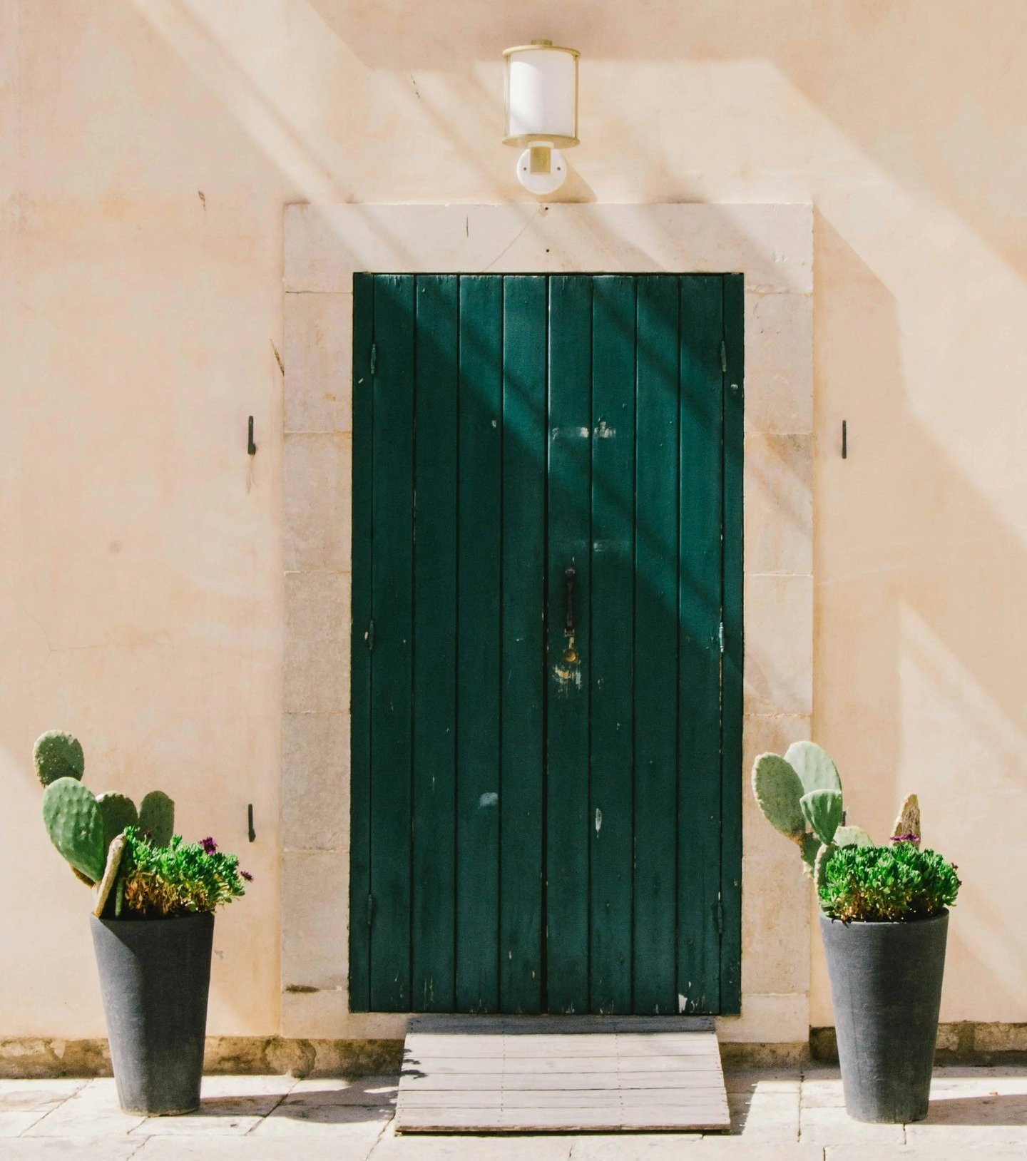 itahome luxury Rustic dark green wooden door on a beige stone wall flanked by potted cactus plants.