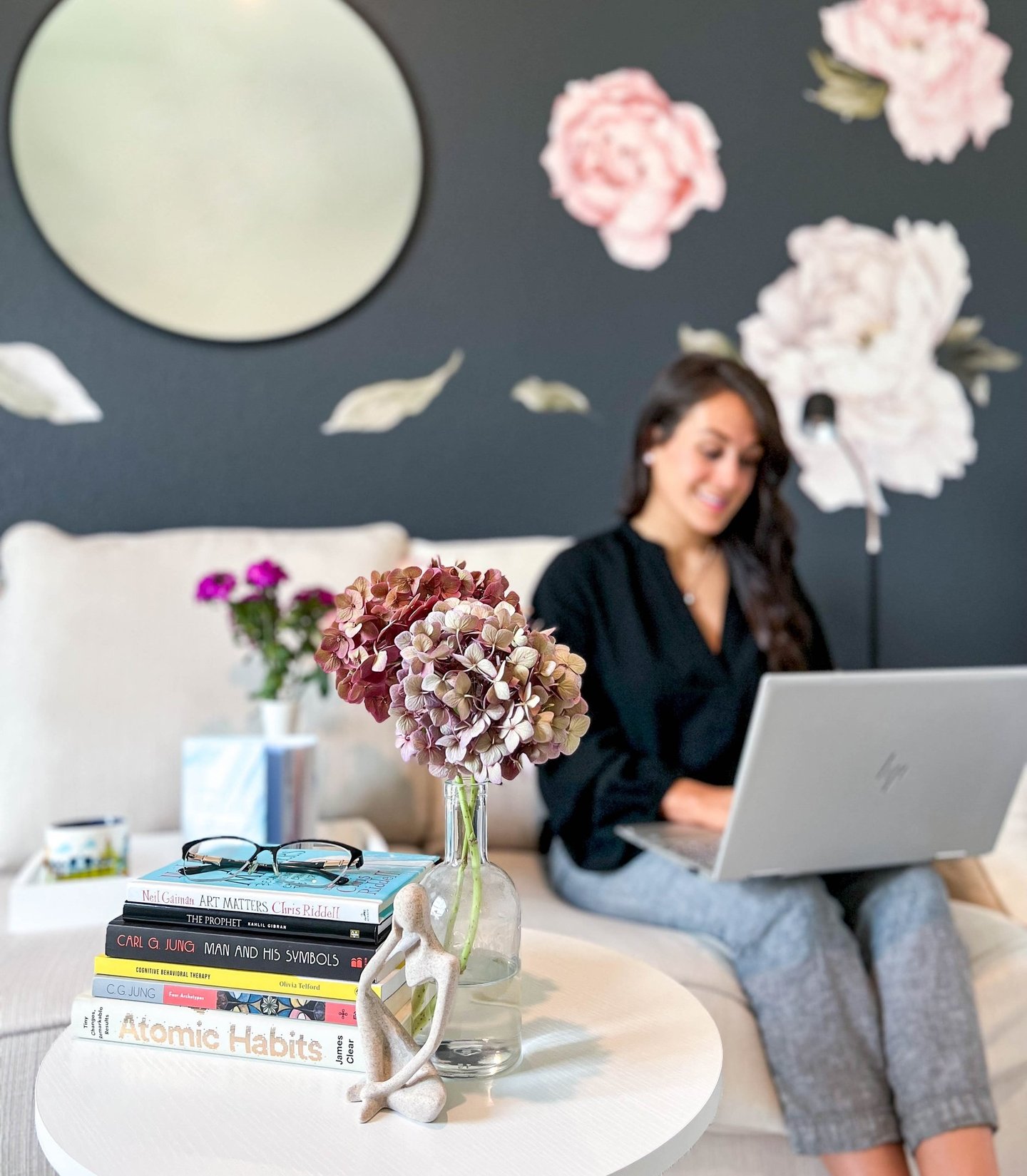 Woman sitting on a couch typing on a laptop with a stack of books nearby