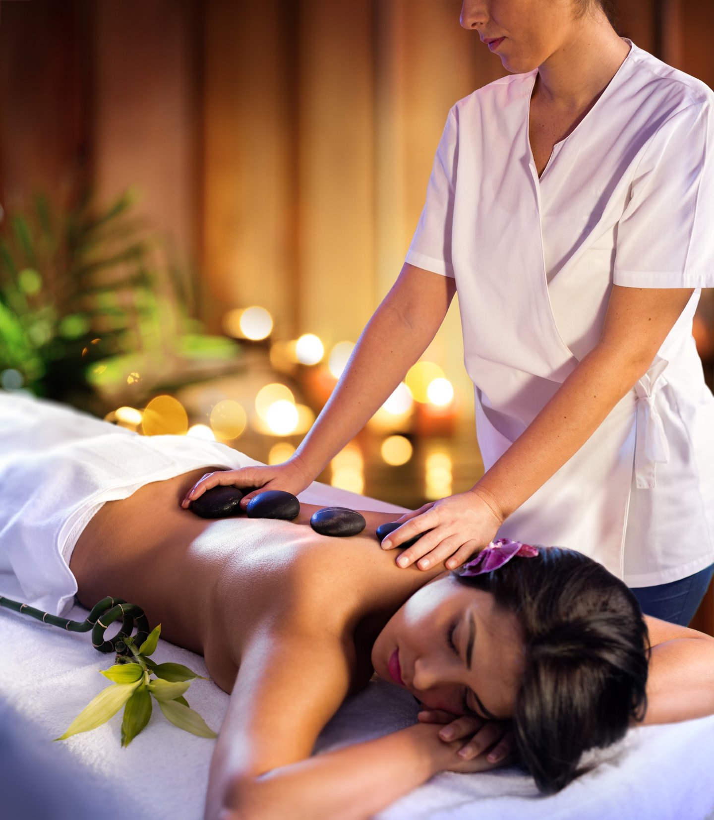 Professional massage therapist performing a hot stone massage treatment for a woman at a luxury spa.