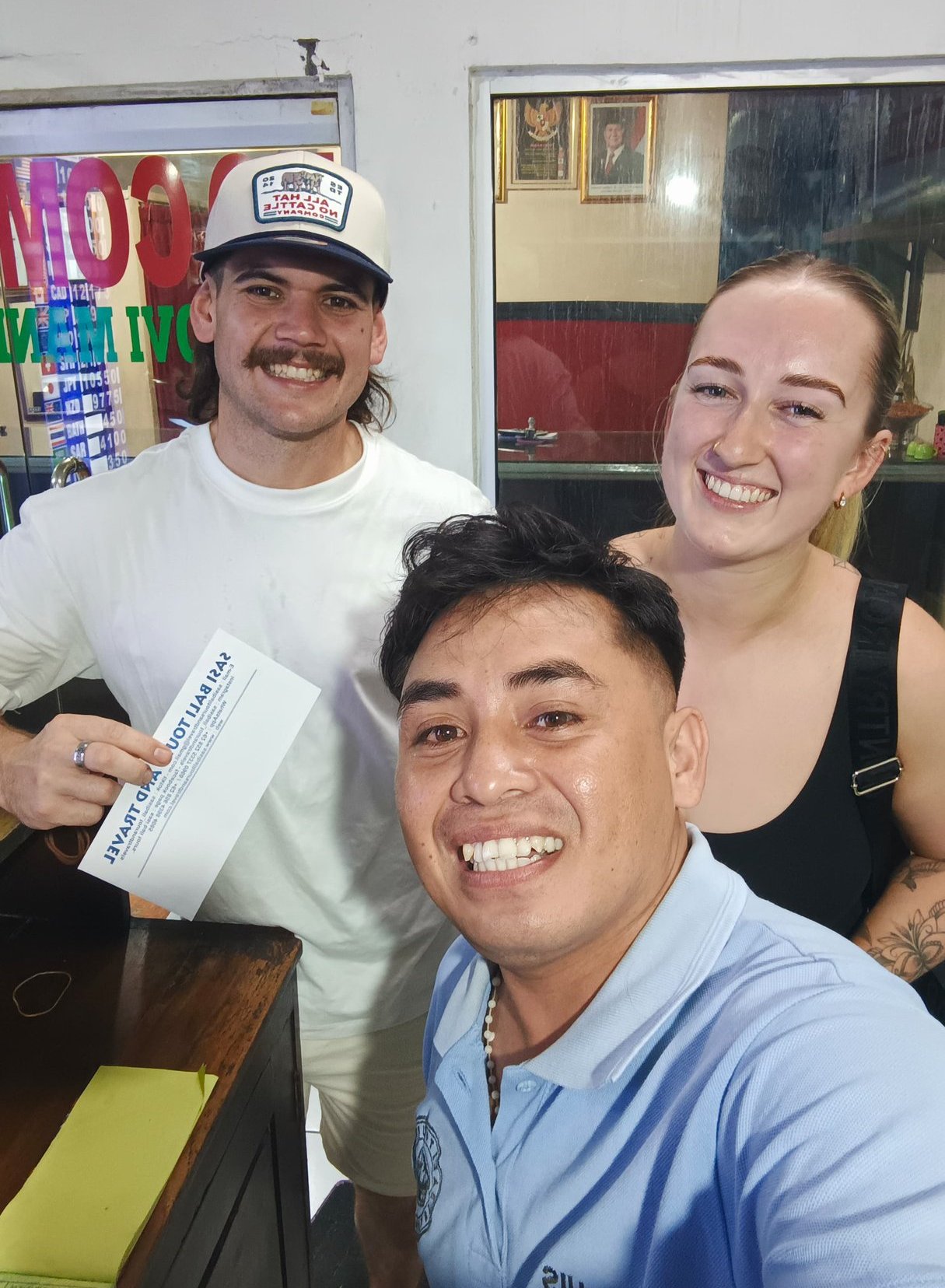 A happy group of travelers posing with a Bali tour voucher at a local travel agency.