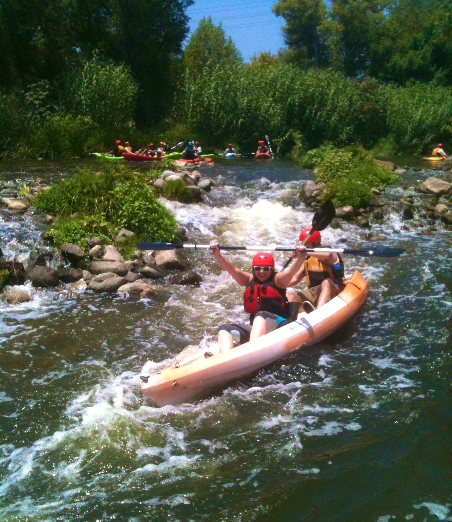 Two people cheering and kayaking through whitewater rapids on a rocky stretch of river.