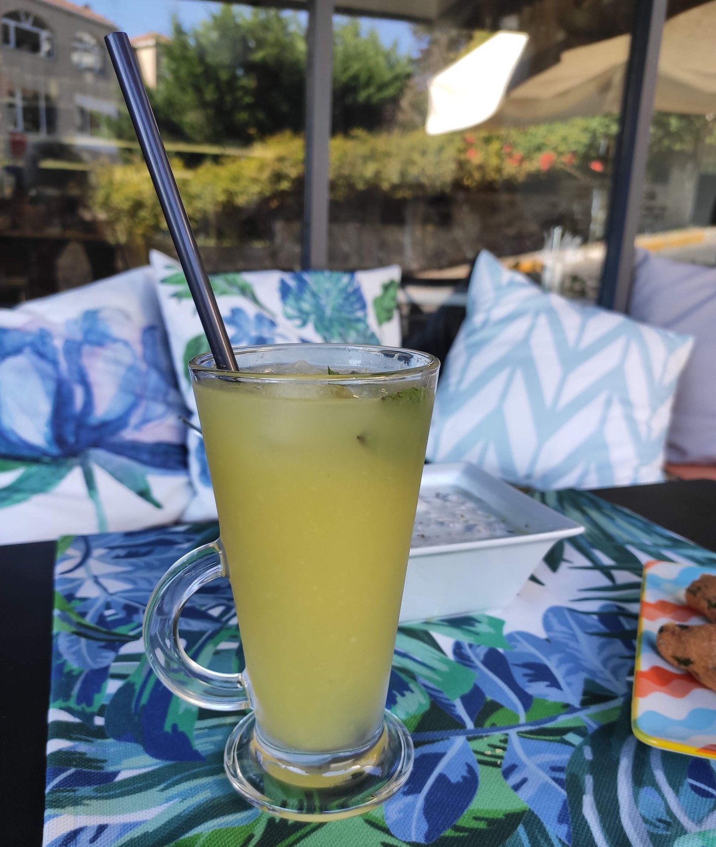 A refreshing glass of homemade lemonade with condensation droplets, set against the cafe’s soft pastel exterior.