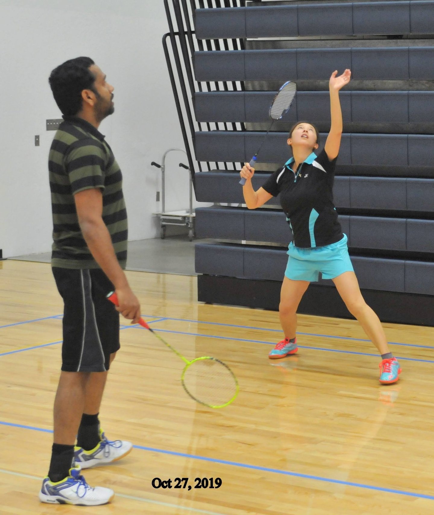 Ellen  preparing to serve during a badminton match in an indoor gym.