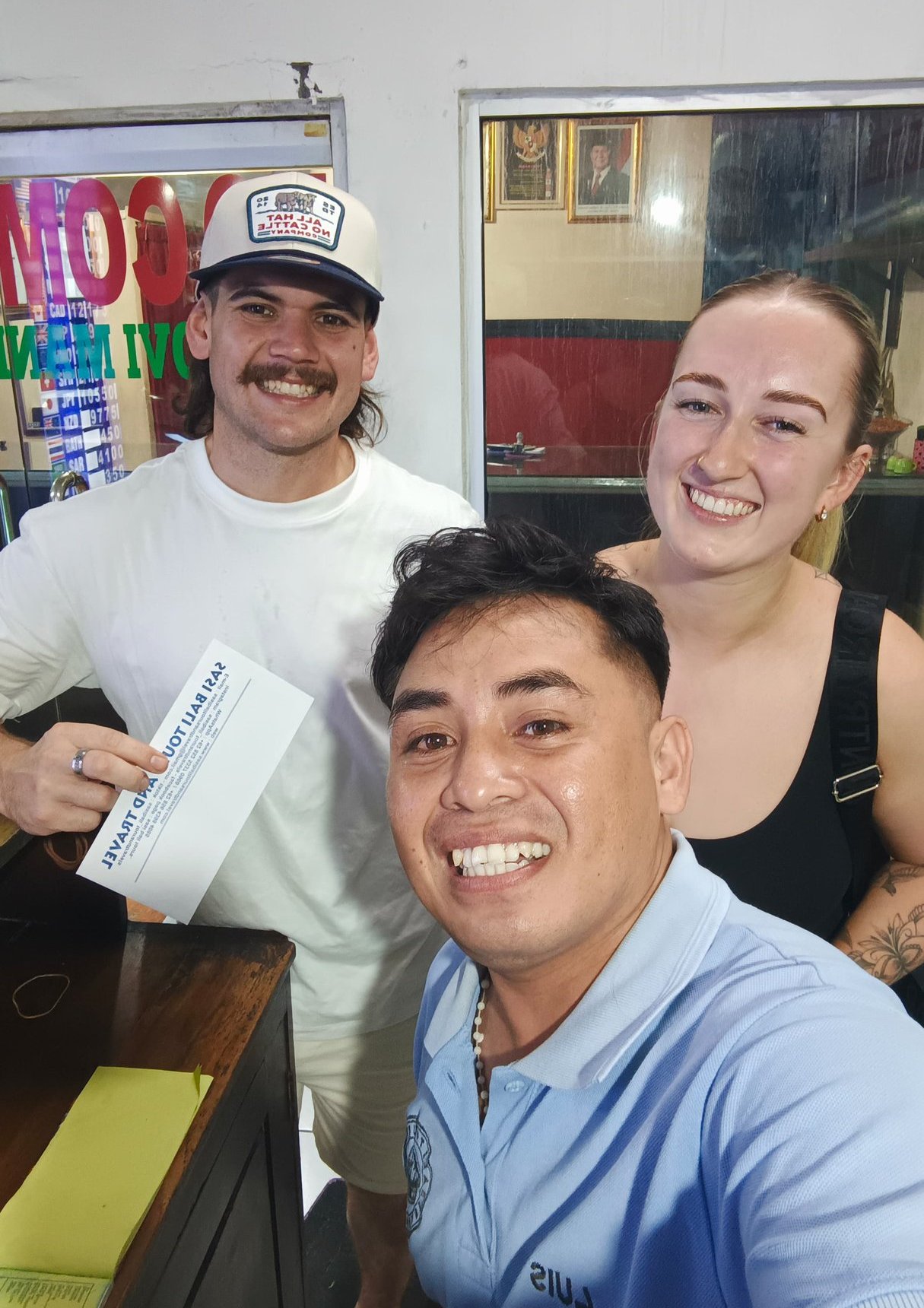 A happy group of travelers posing with a Bali tour voucher at a local travel agency.