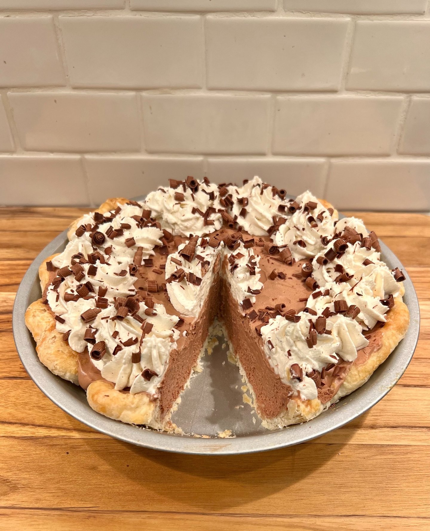 A homemade chocolate silk pie with whipped cream and chocolate shavings on a wooden counter.