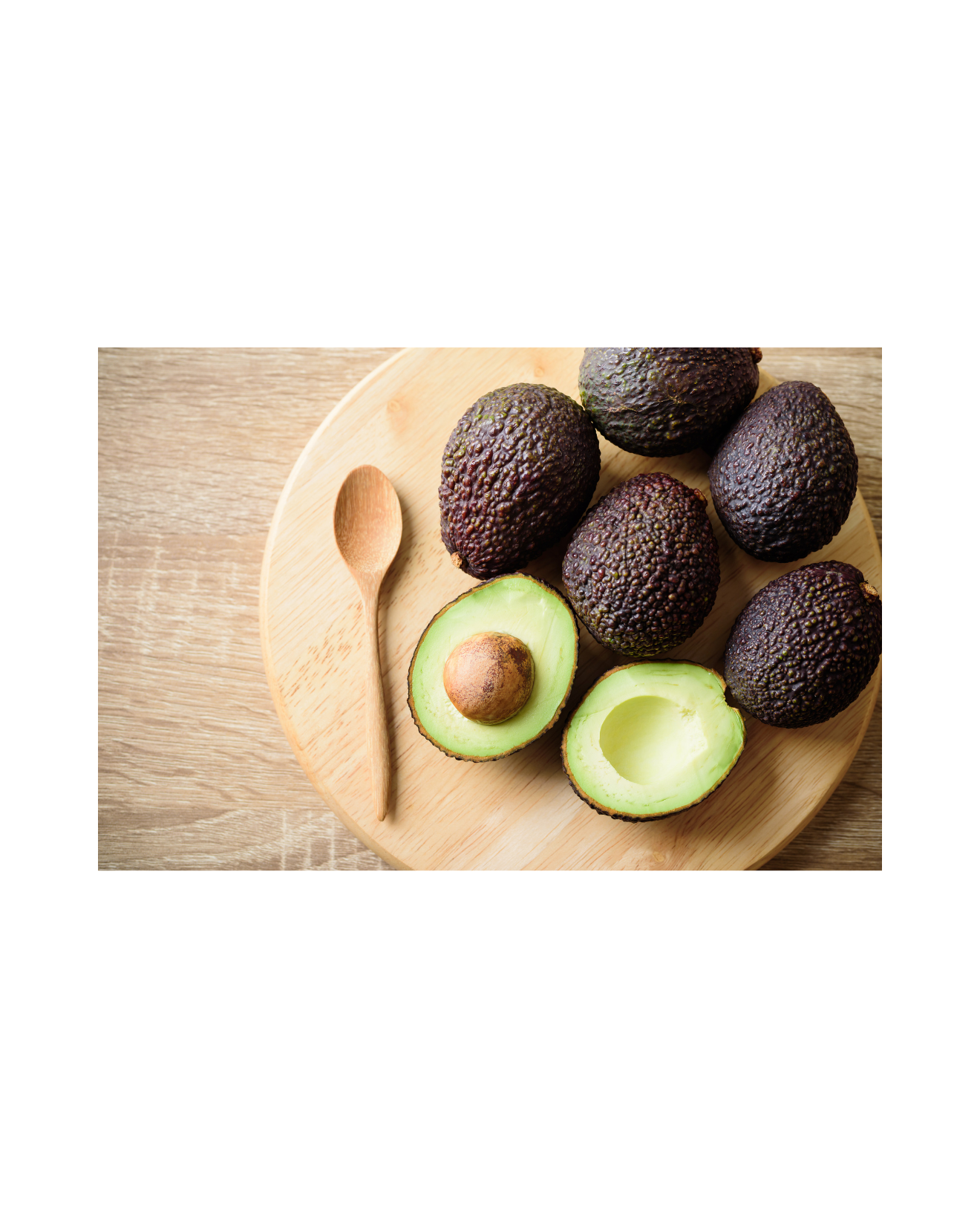 Fresh ripe Hass avocados and a wooden spoon on a circular cutting board for healthy meal prep.