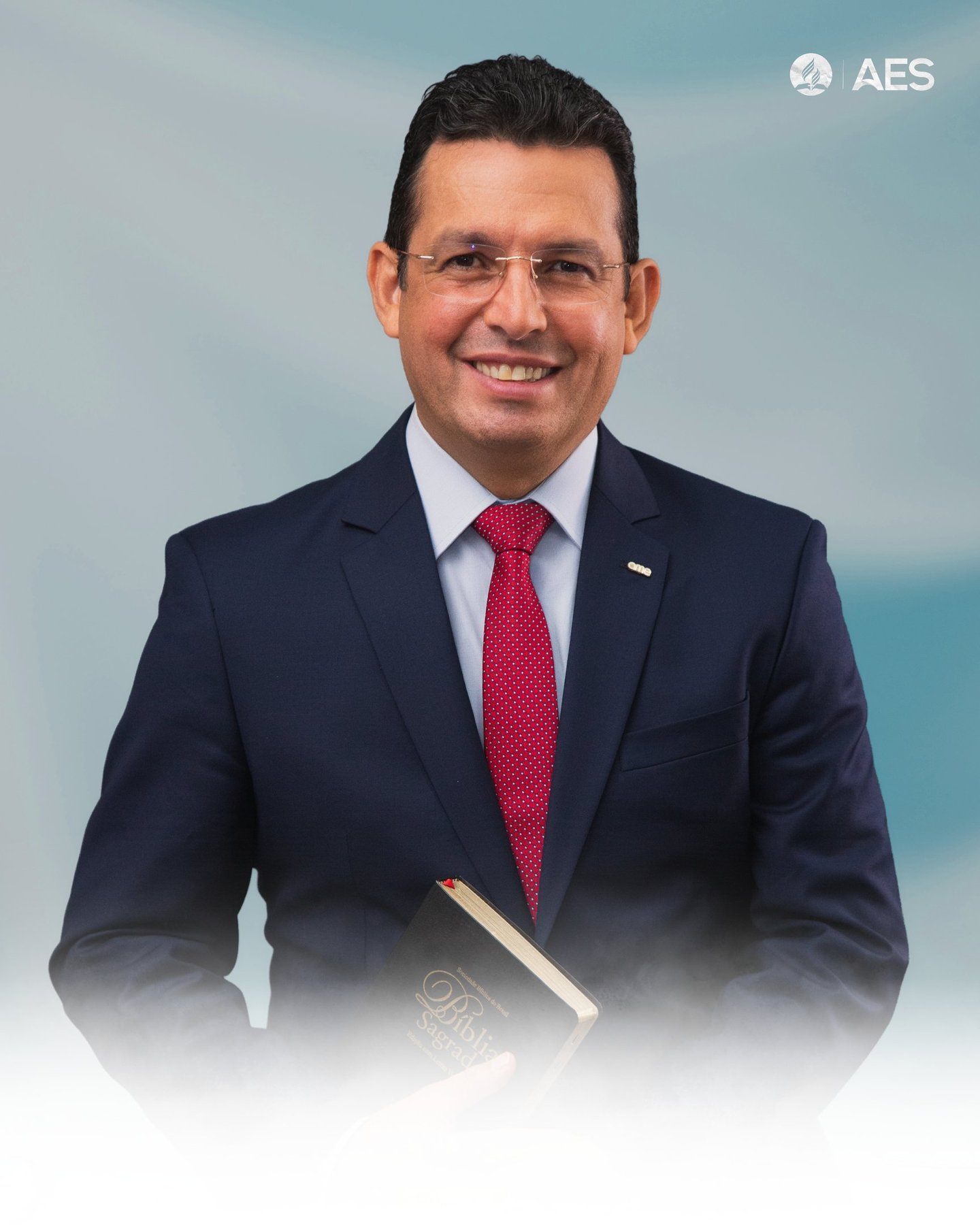 Smiling man in a navy suit and red tie holding a Holy Bible, representing religious leadership.