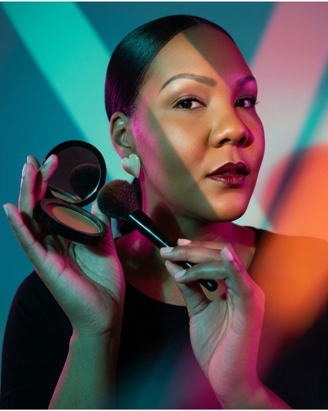 A woman applying makeup with a brush and powder compact against a colorful neon light background.