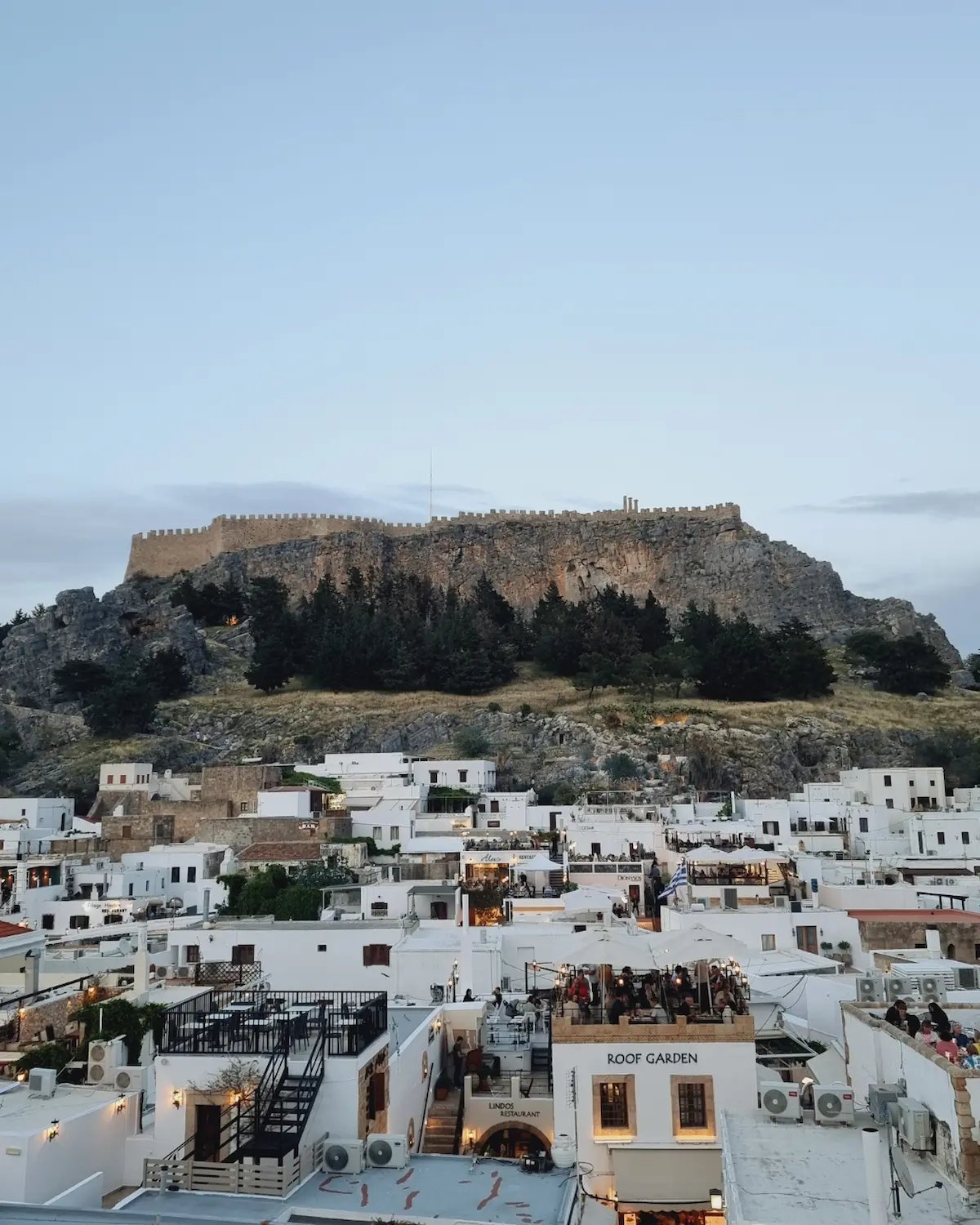 Panoramic view of the Acropolis of Lindos towering over white buildings in Rhodes, Greece.