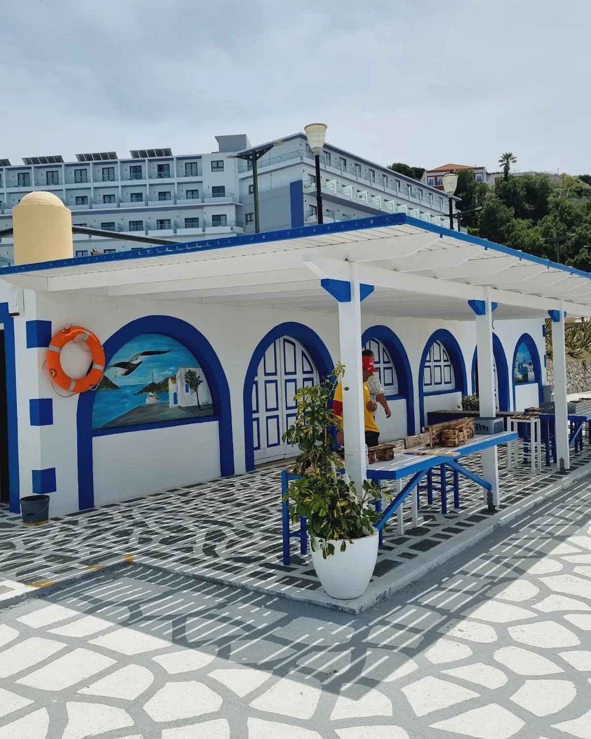 White and blue Greek style seaside building with arched murals and an outdoor patio.