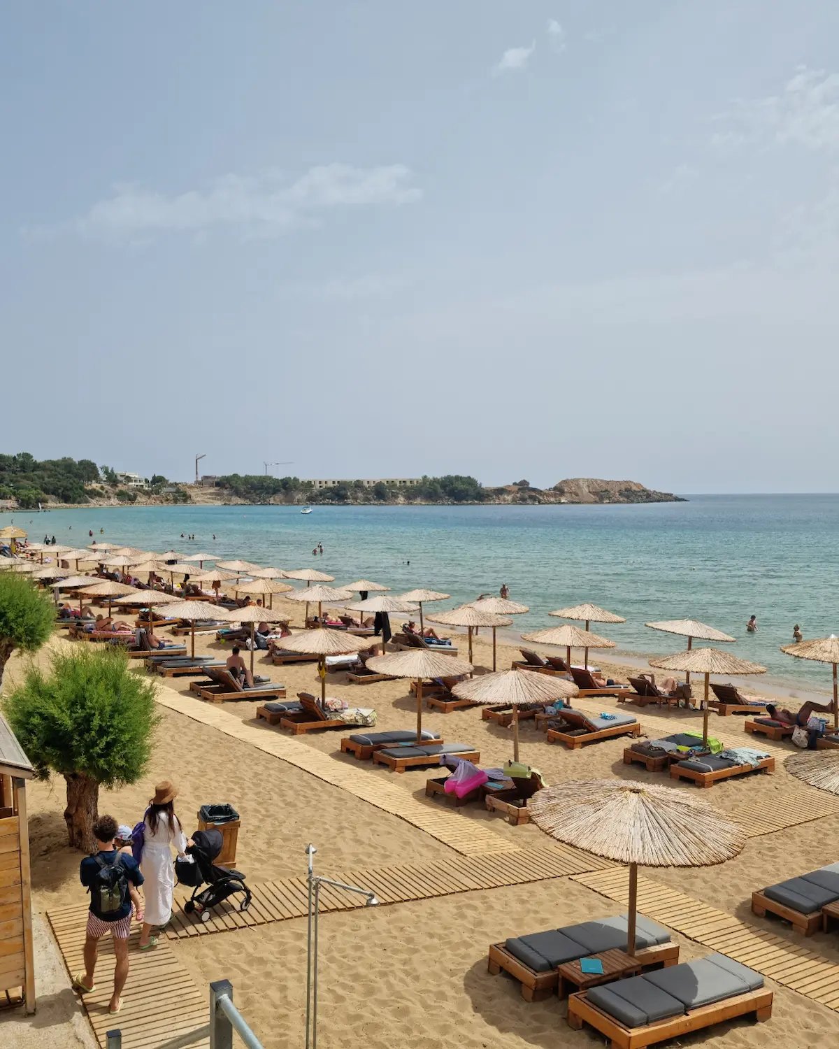 Sunny beach resort in Greece with straw umbrellas, wooden loungers, and turquoise Mediterranean water.