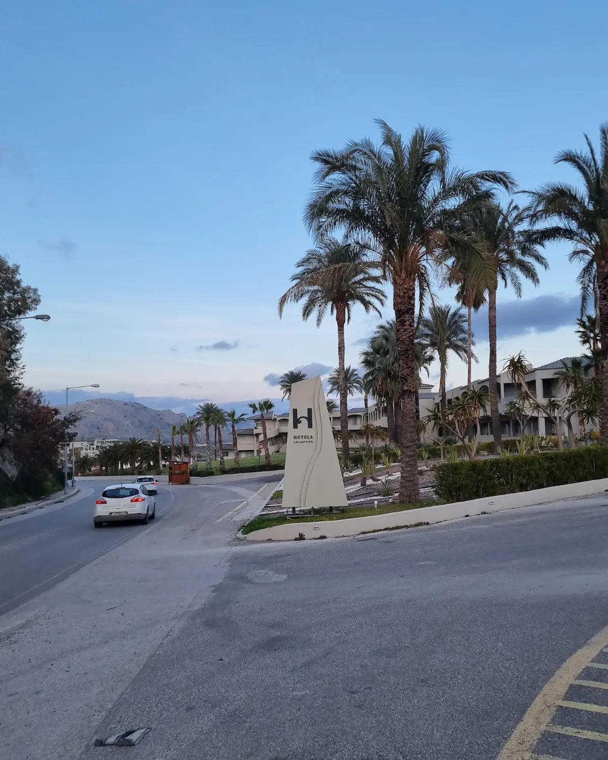 Luxury resort entrance with palm trees and modern signage along a scenic coastal road.