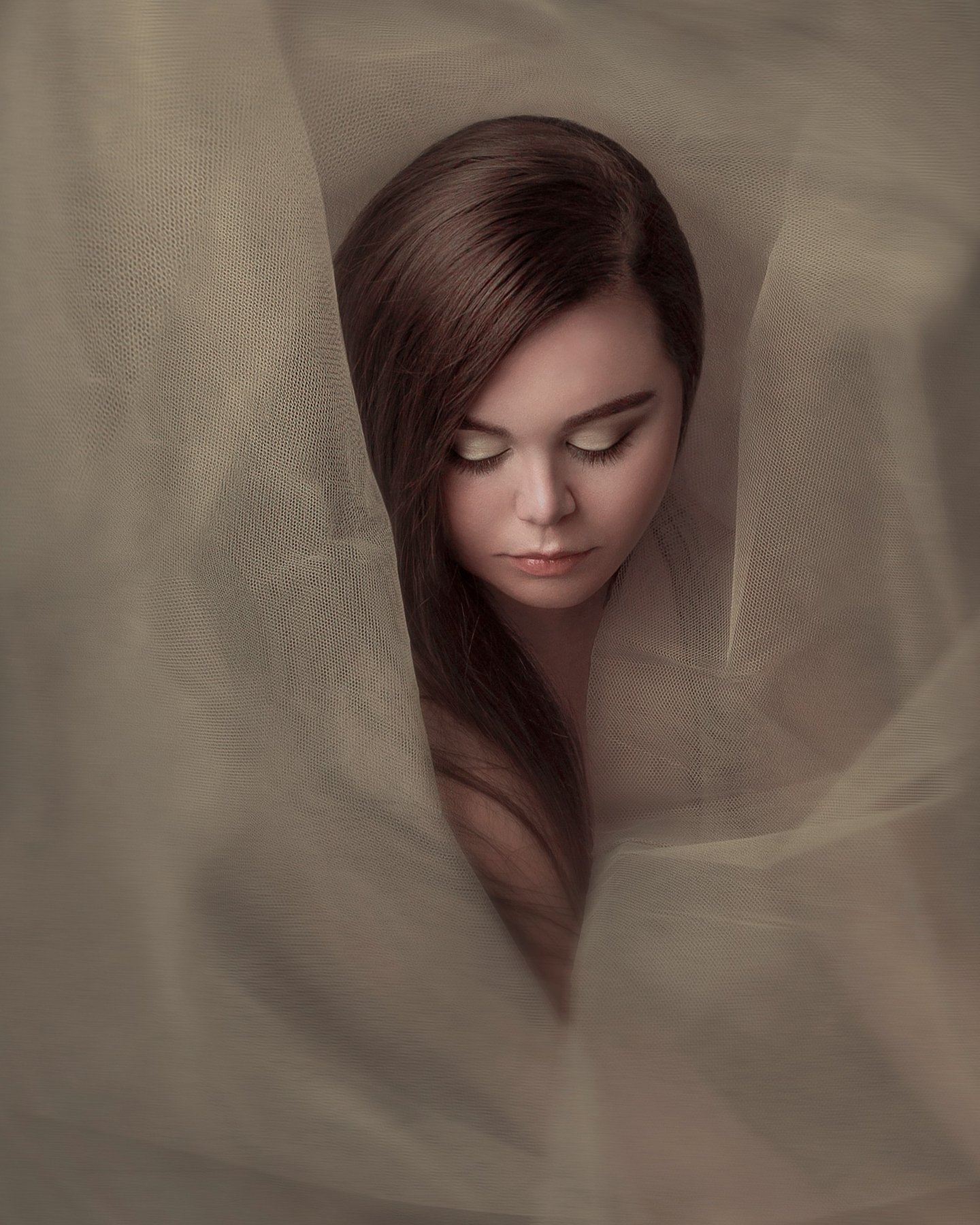 Creative portrait of a young woman wrapped in sheer tulle, creating an ethereal, dreamy effect.