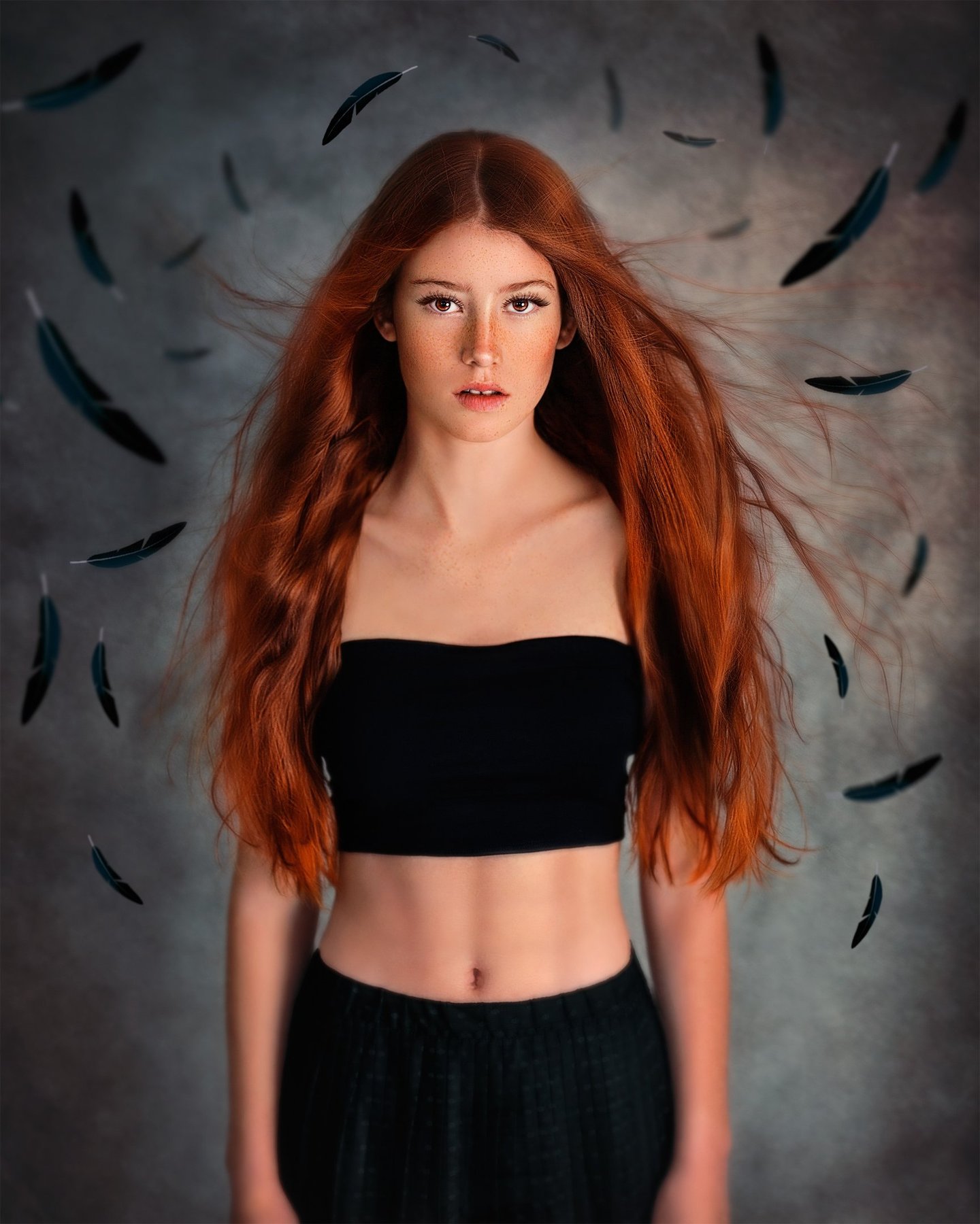 red head girl with freckles, wearing black skirt and crop top. Black feathers around her