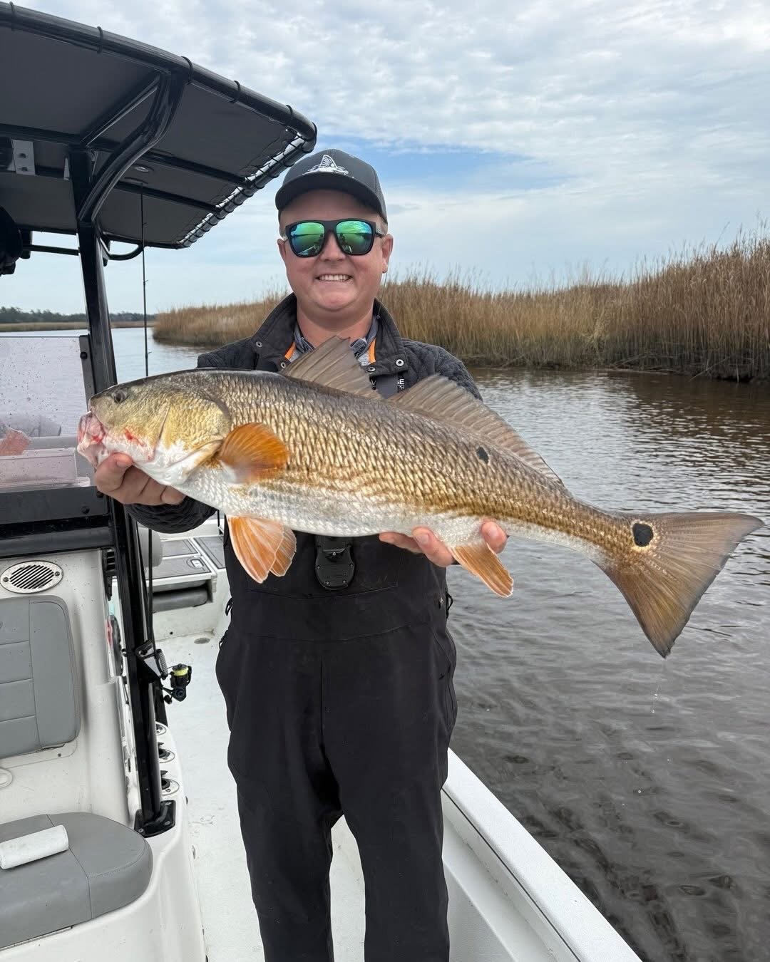 Will Bonniville holding a red drum in a coastal marsh while fishing from a boat