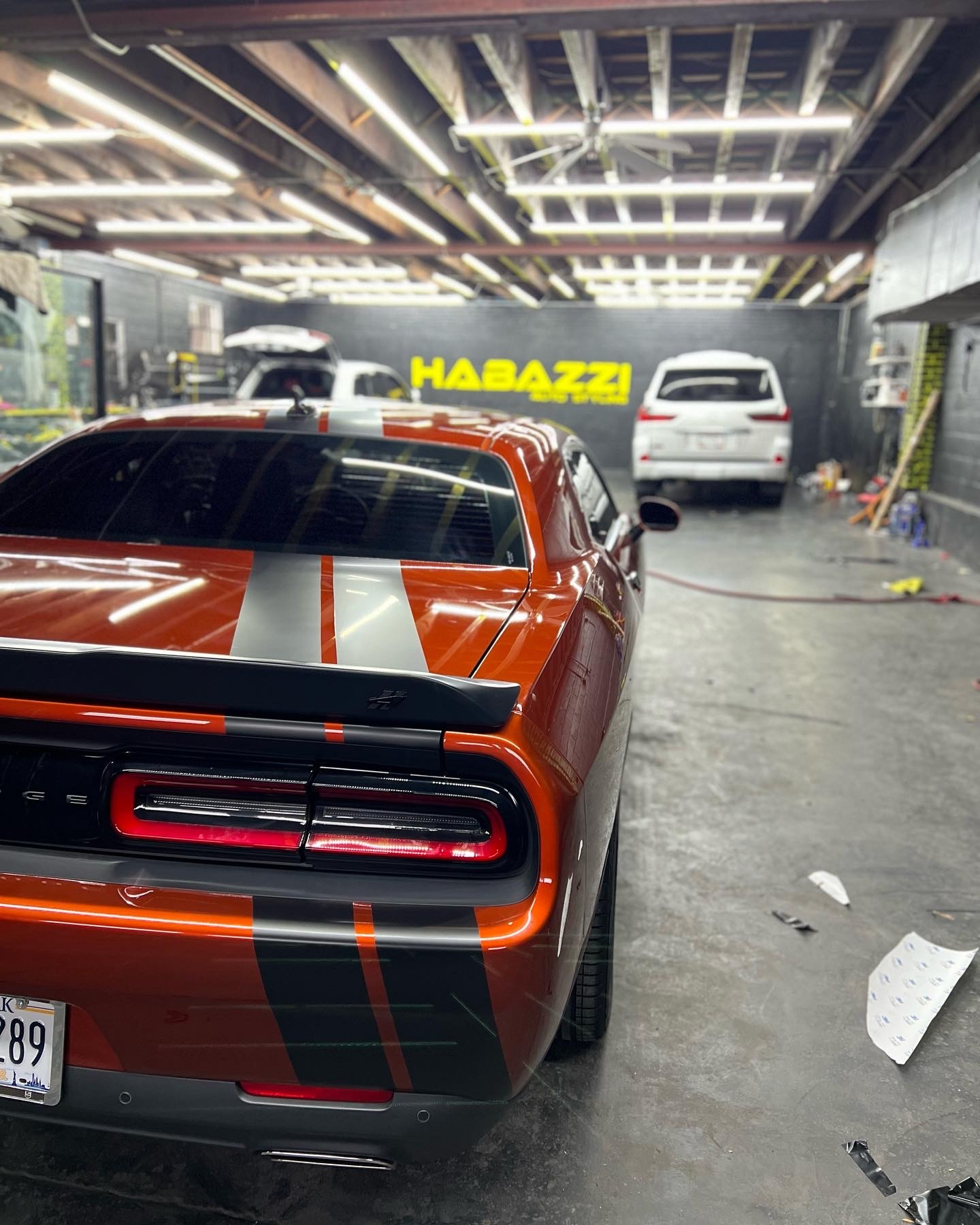Orange Dodge Challenger with black racing stripes undergoing custom vinyl wrap at Habazzi Auto Styles garage.