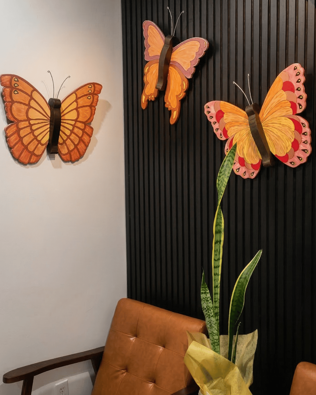 Modern interior wall decor featuring orange butterfly art on black wood slats and a snake plant.