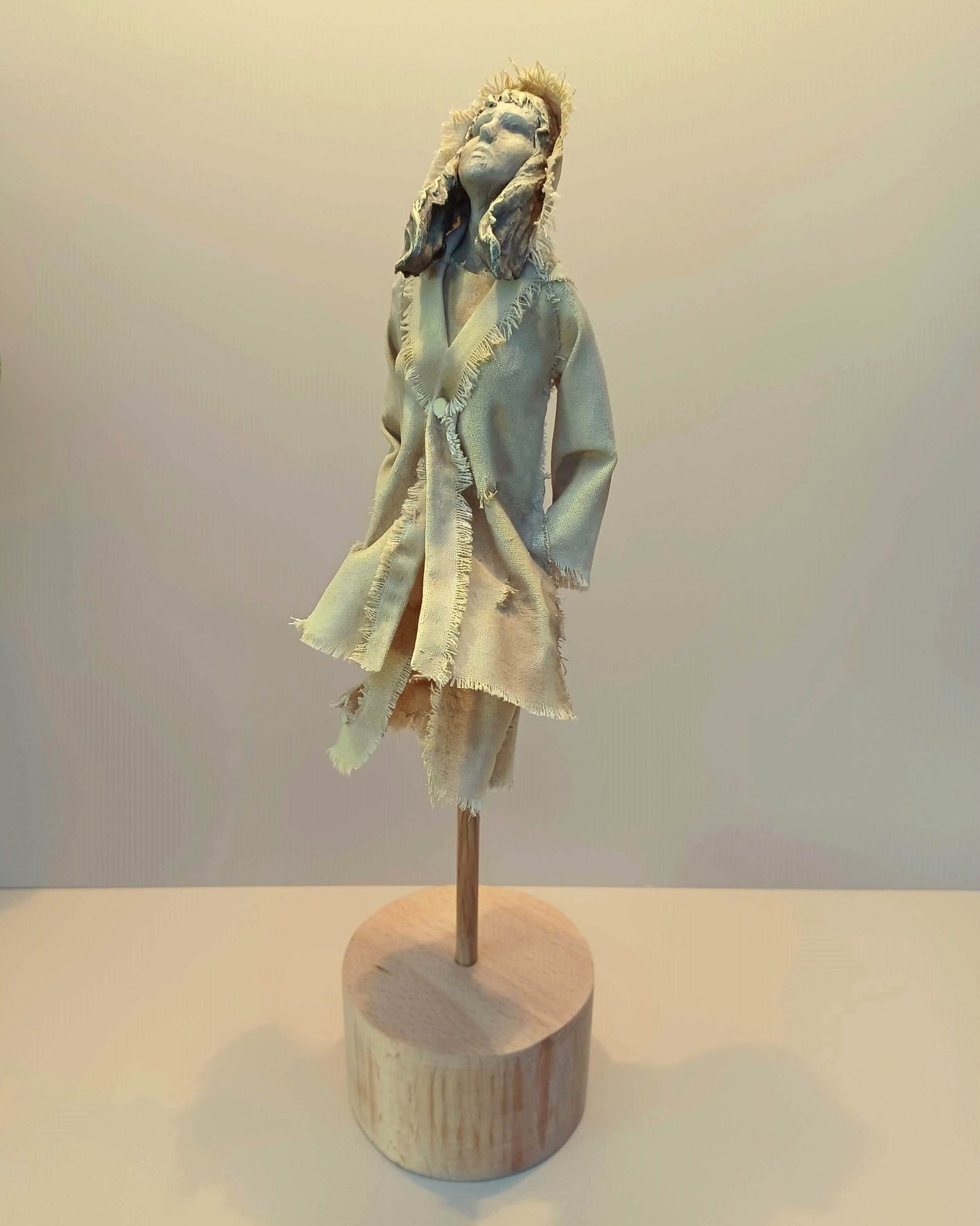 Clay and canvas sculpture of a female figure gazing upwards, wearing windswept, ragged clothes.