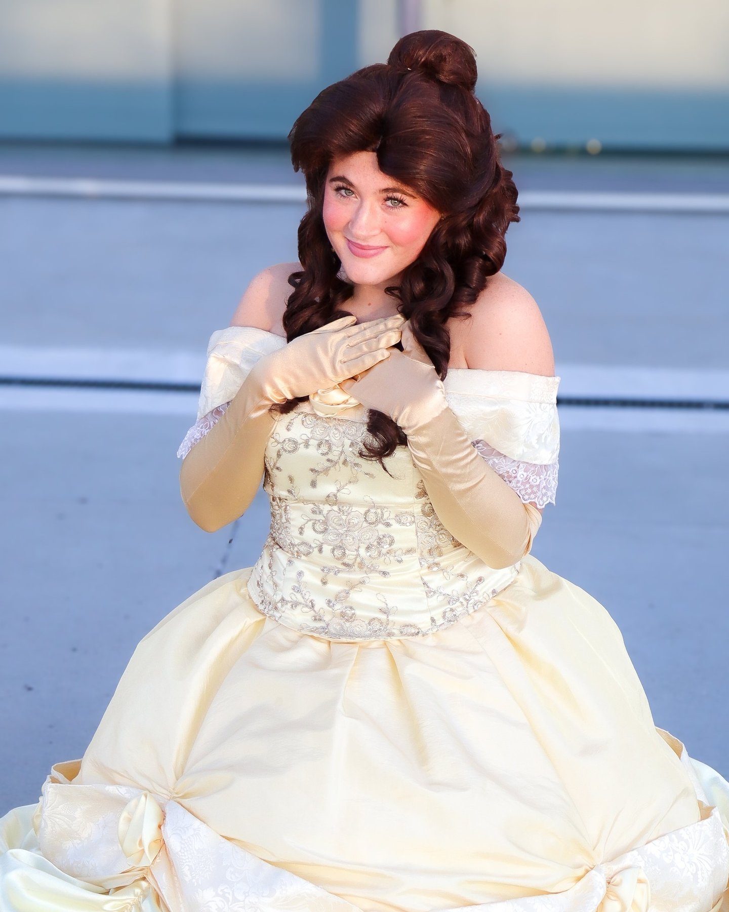 A woman in a Belle cosplay costume with a yellow ballroom gown and long gold gloves.