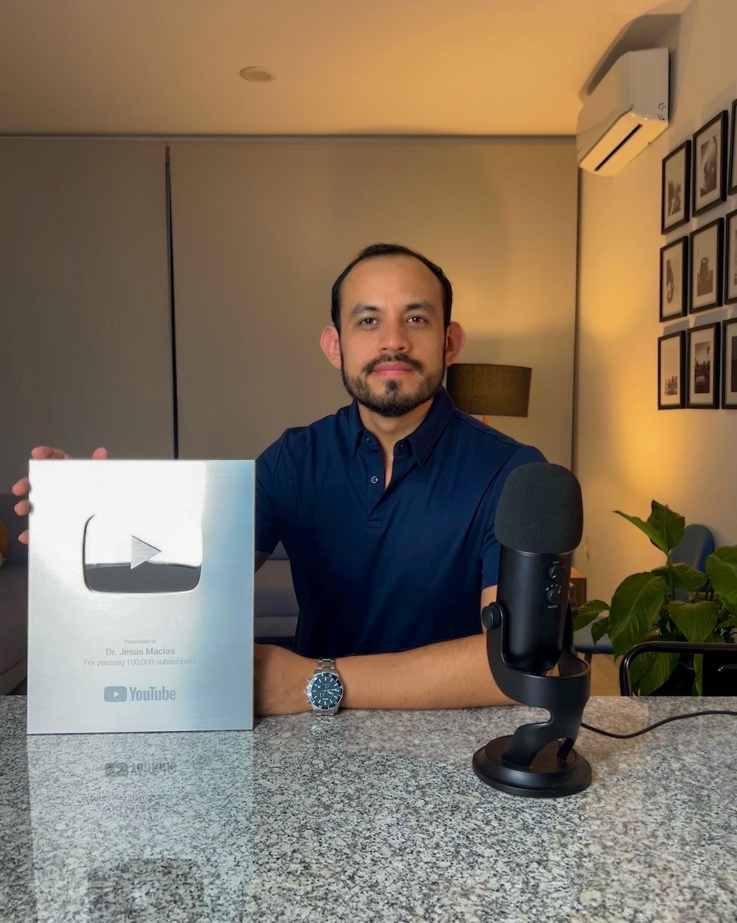 Content creator Dr. Jesús Macías holding a Silver YouTube Creator Award for 100k subscribers in a studio.