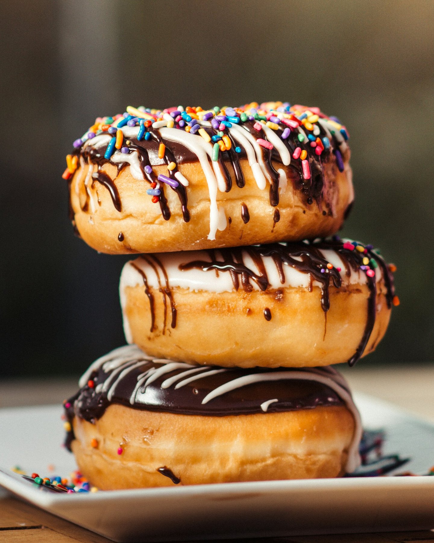 three stacked donuts with white glaze and chocolat coat and colorful sprinkles